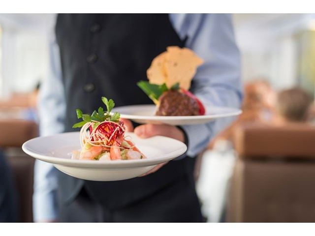 A server holds to dishes with elegantly plated food.