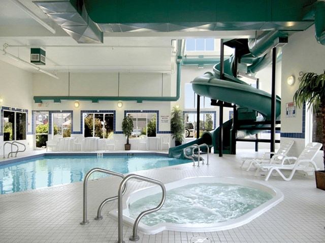 Indoor pool at Canalta Brooks with slide, hot tub, lounge chairs, and large windows.