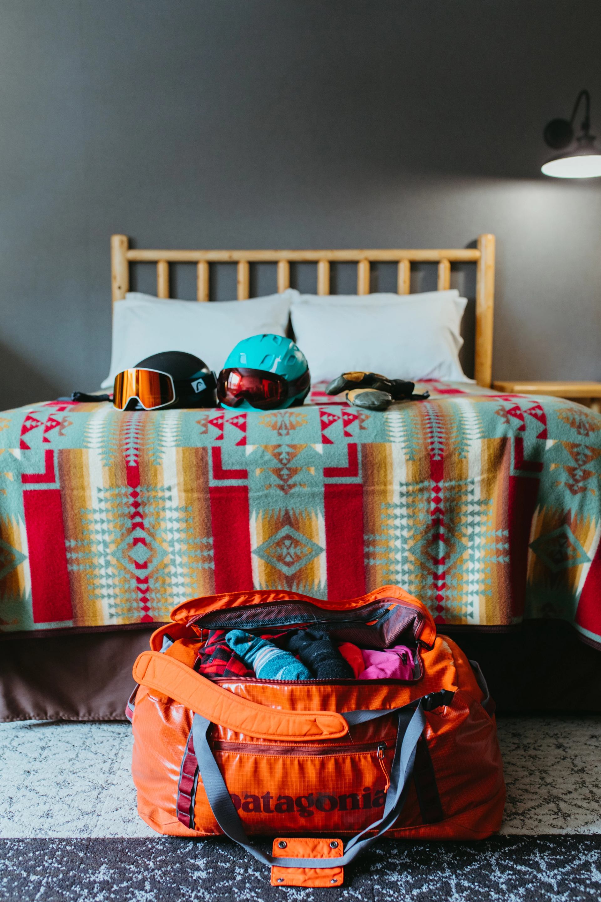 Lodge room with patterned bedding, gear on bed, and open duffel bag on the floor.