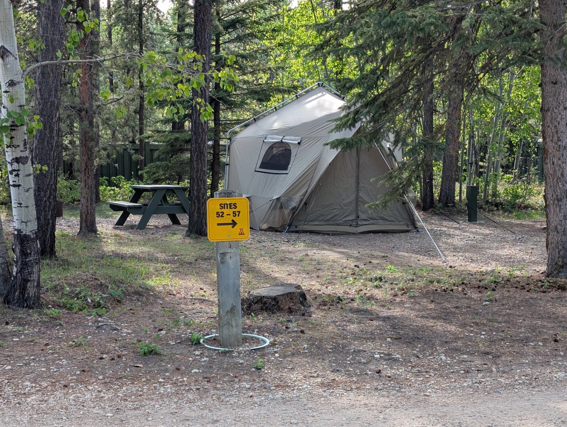 Campsite with large canvas tent, picnic table and yellow sites 52–57 sign among trees.