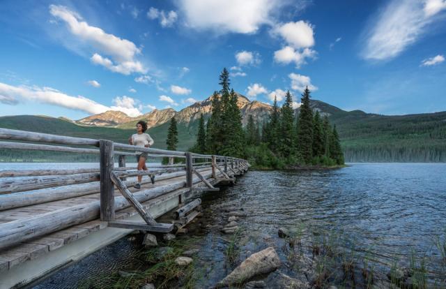 A women running across a bridge surrounded by water at Pyramid Lake in Jasper National Park.