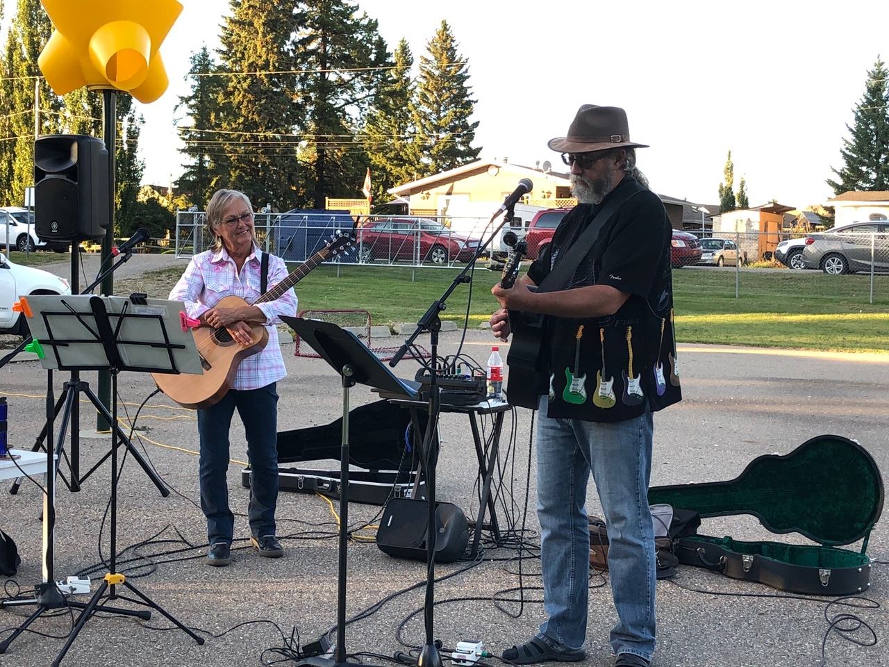 A man and woman with guitars and microphones perform an outdoor concert.