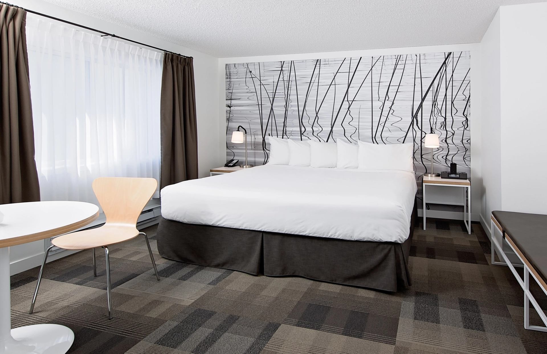 Modern hotel room with tree-themed wall art, cozy seating, and soft lighting.