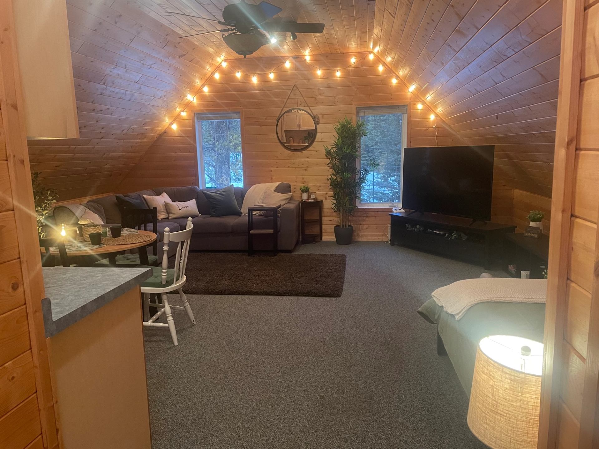 Warm studio loft with bed, seating area, dining table, and string lights.