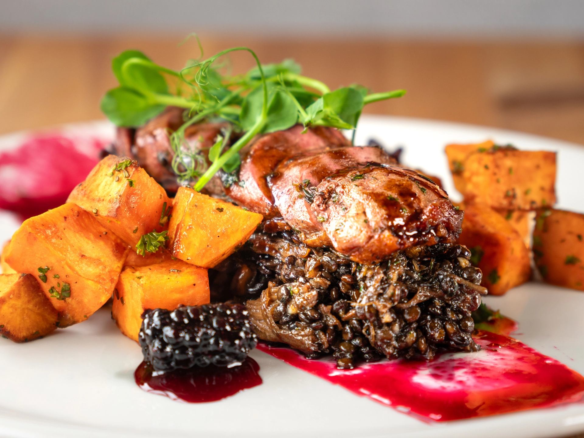 Gourmet dish with meat, sweet potatoes, berries, and microgreens.