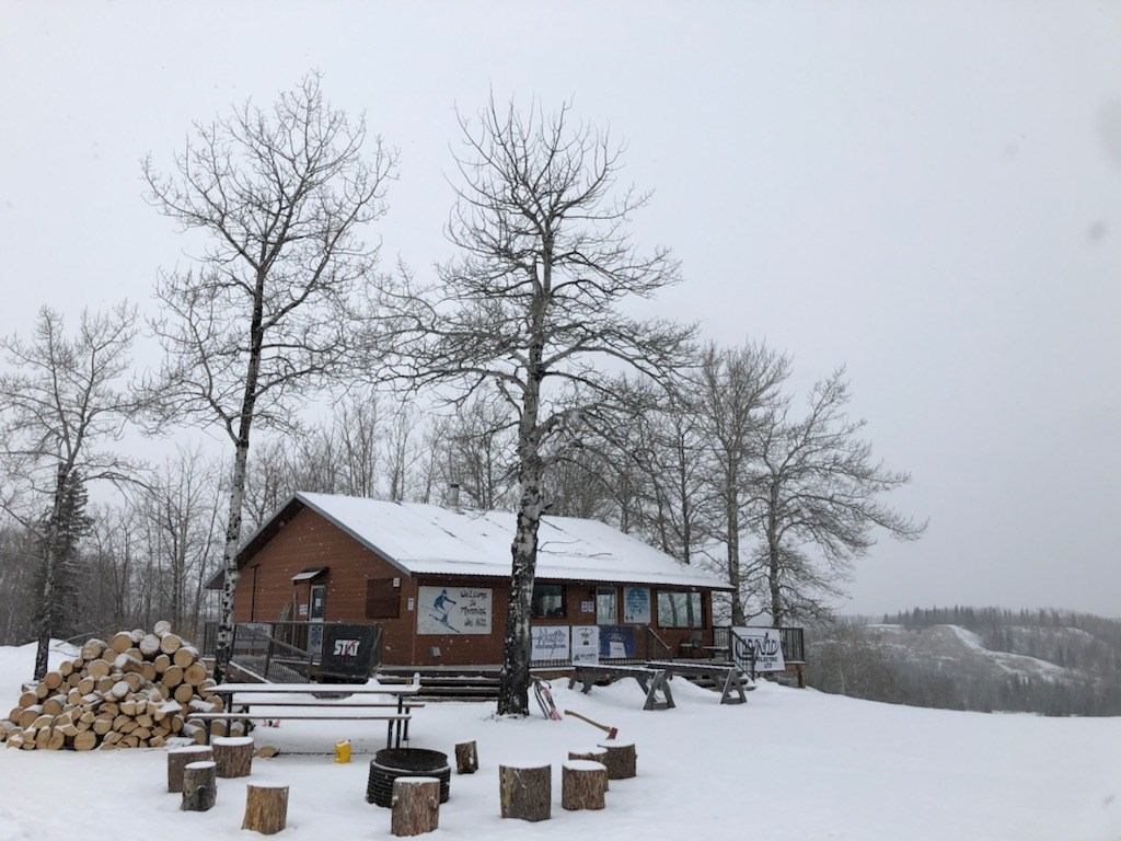 Snowy cabin with firewood and benches in a quiet winter forest.