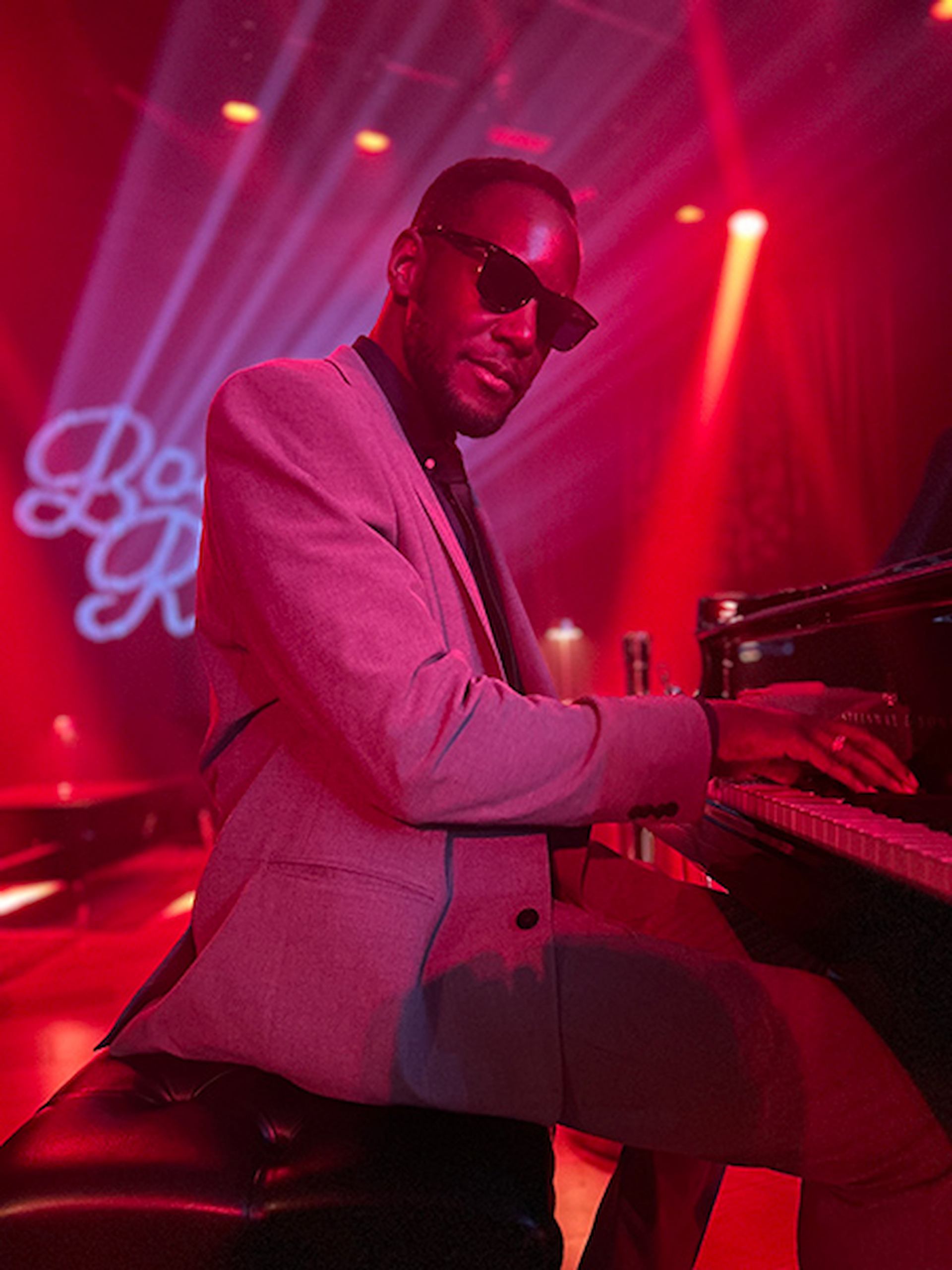 Timothonius playing the piano with red lighting behind him.