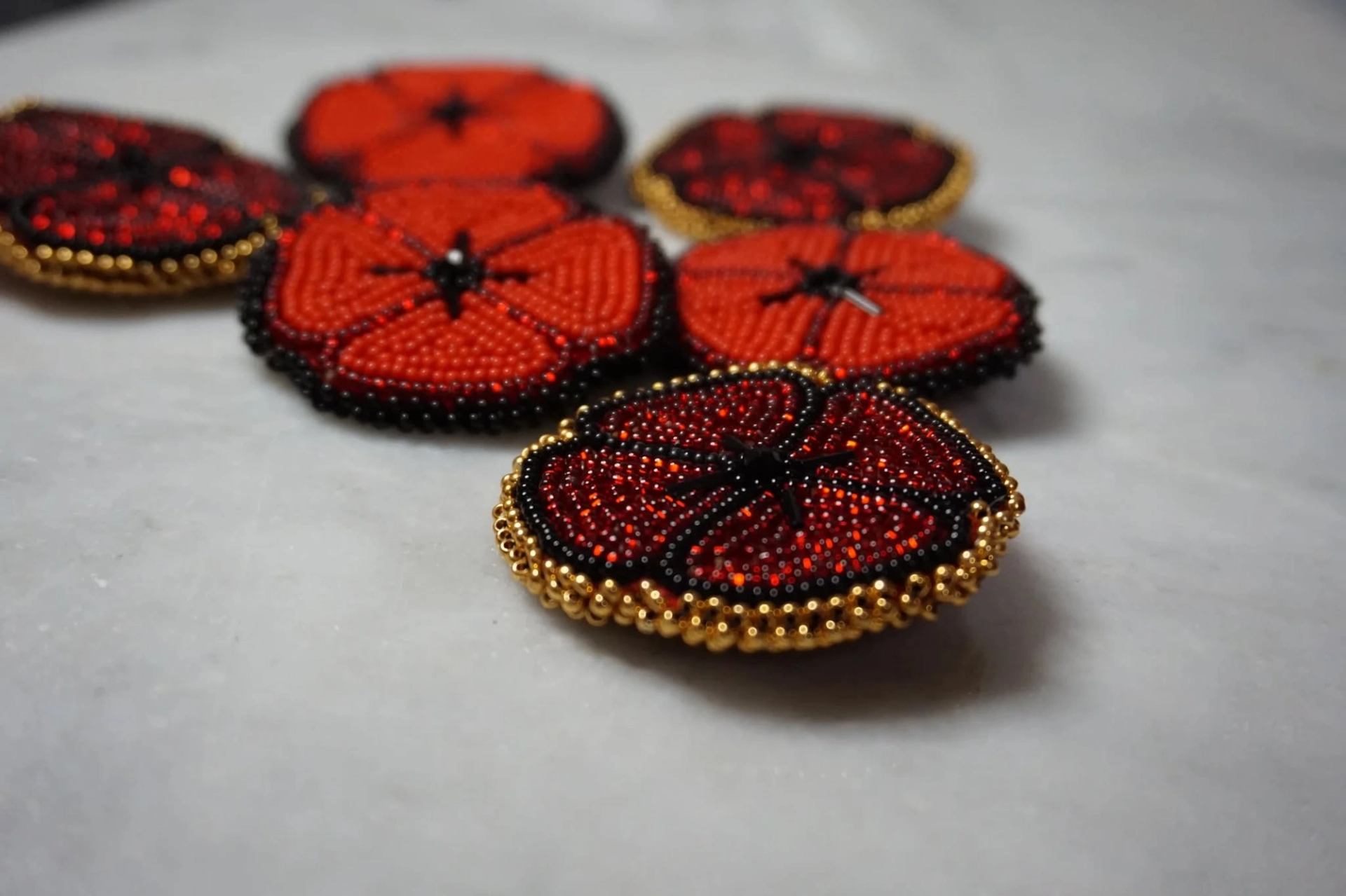 Beaded red and black flower-shaped pins with gold edges arranged on a light surface.