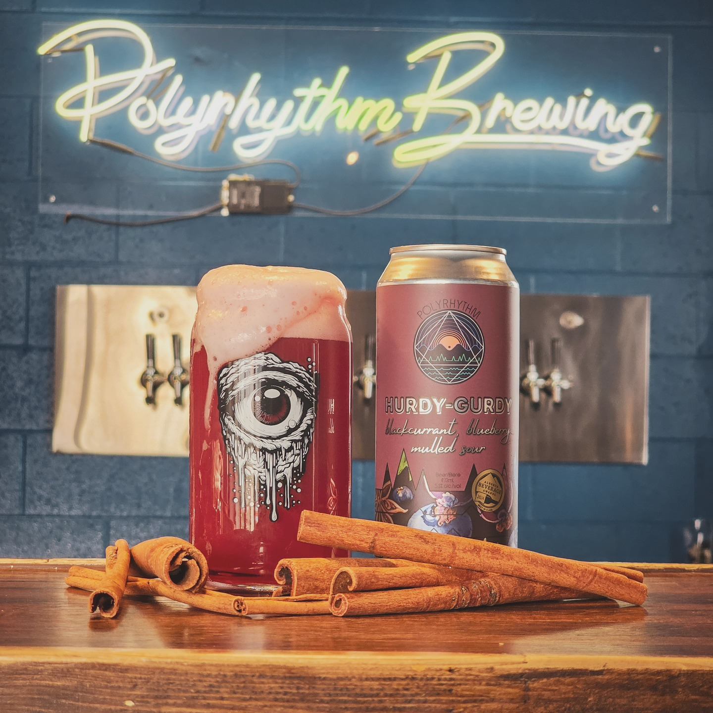 Foamy red beer and Hurdy‑Gurdy can on bar with cinnamon sticks and neon sign