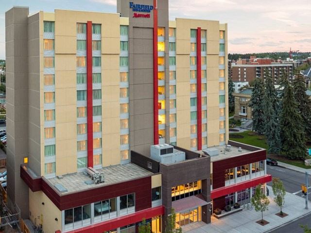 Modern hotel with beige-red facade, large windows, and landscaped entrance.
