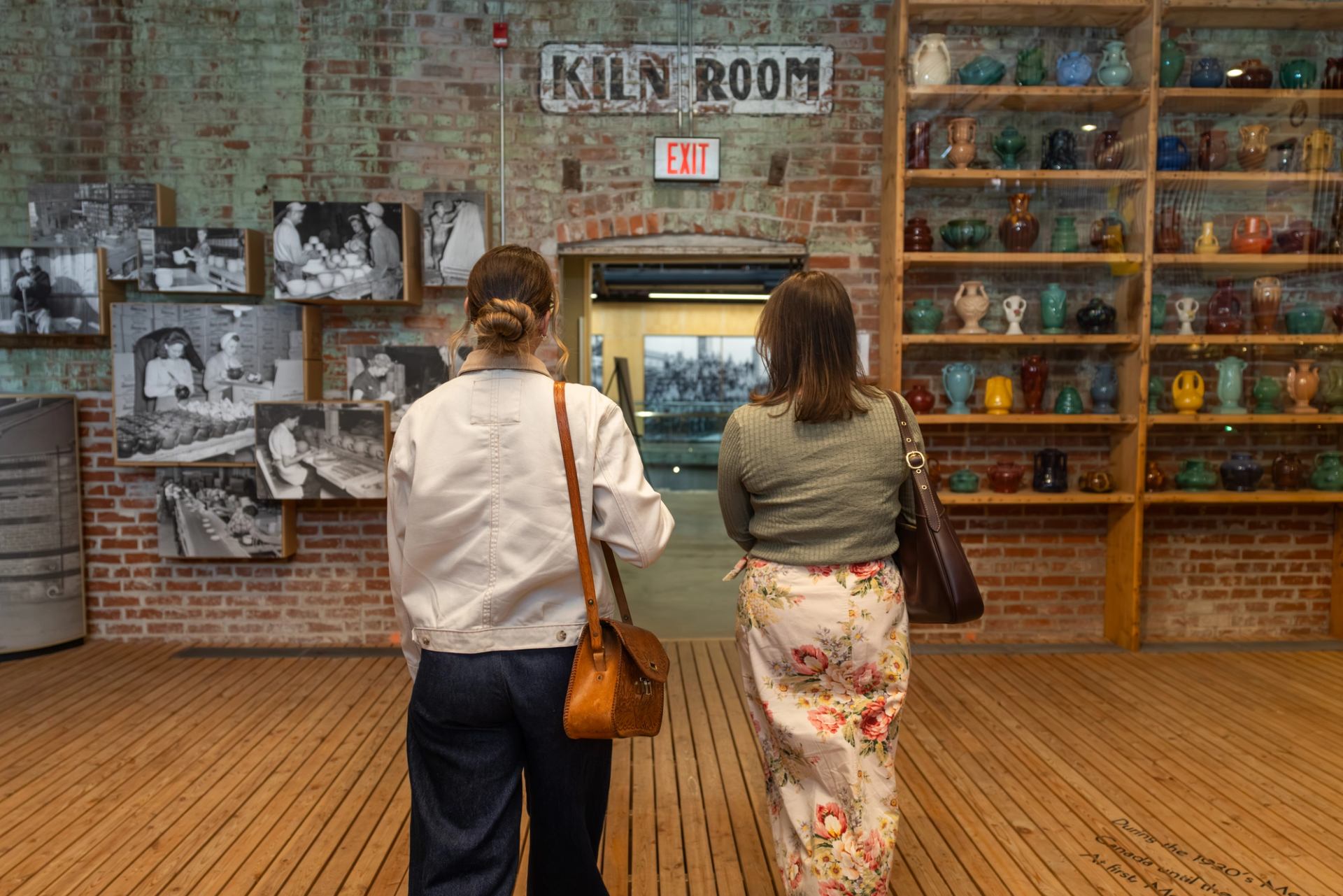Visitors view historic photographs and colourful pottery displays in a brick-walled gallery.