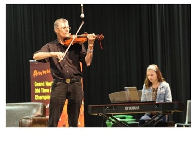 Violinist performs on stage beside keyboard player seated at Yamaha piano.