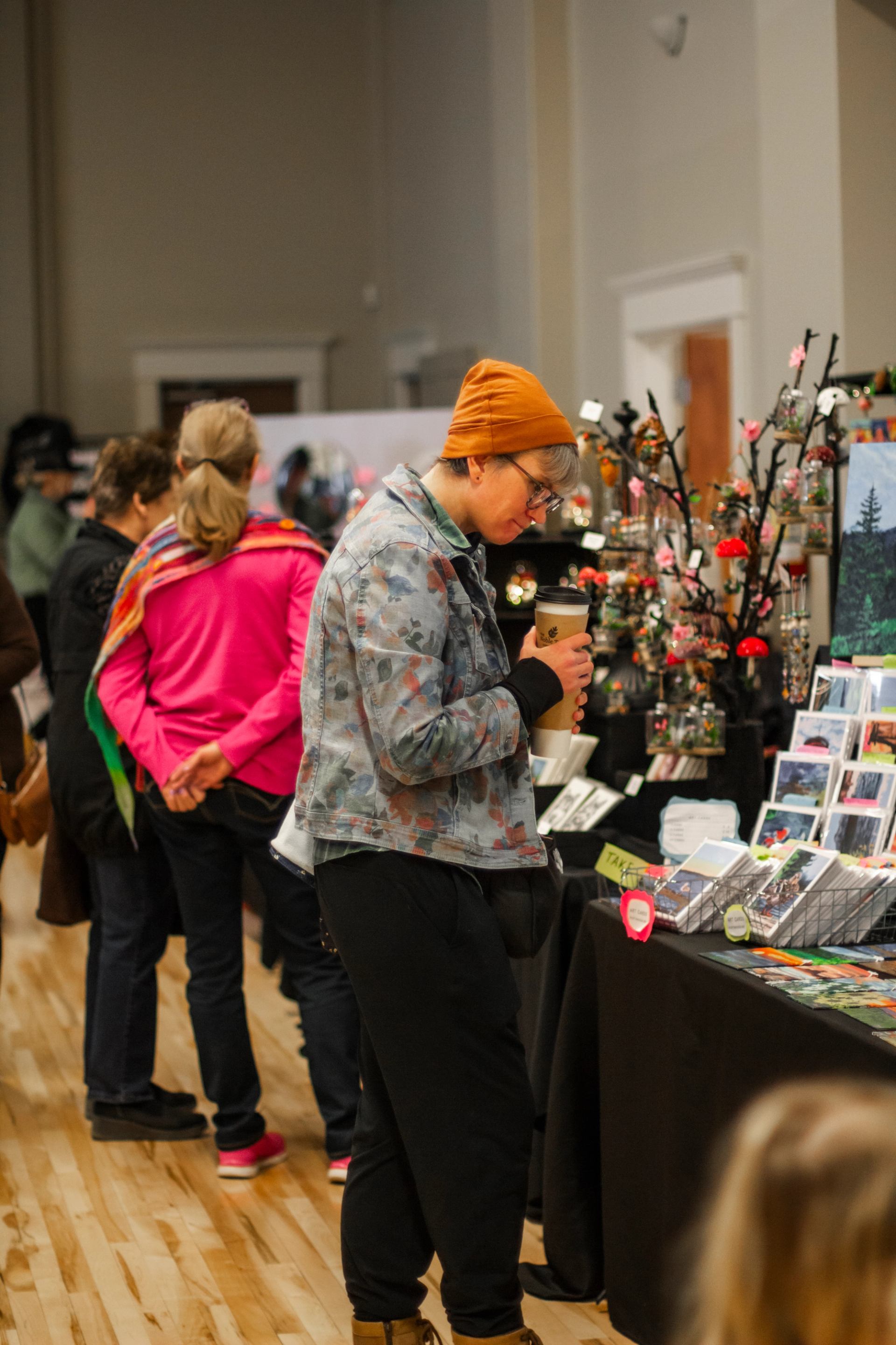 People browse tables of handmade goods and art at an indoor market celebrating International Women’s Day.