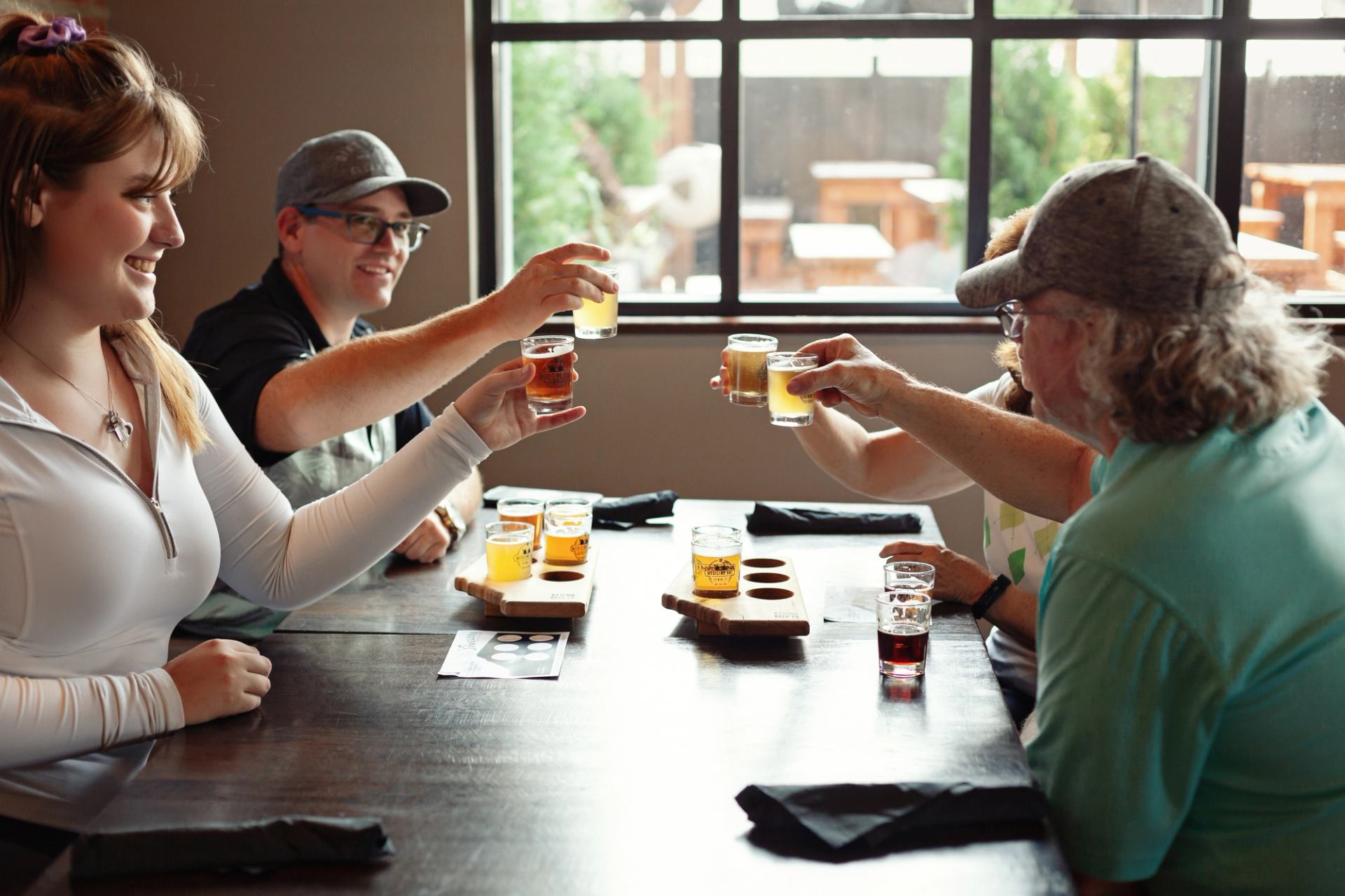 People clinking small tasting glasses at a wooden table during a guided drink tasting indoors.