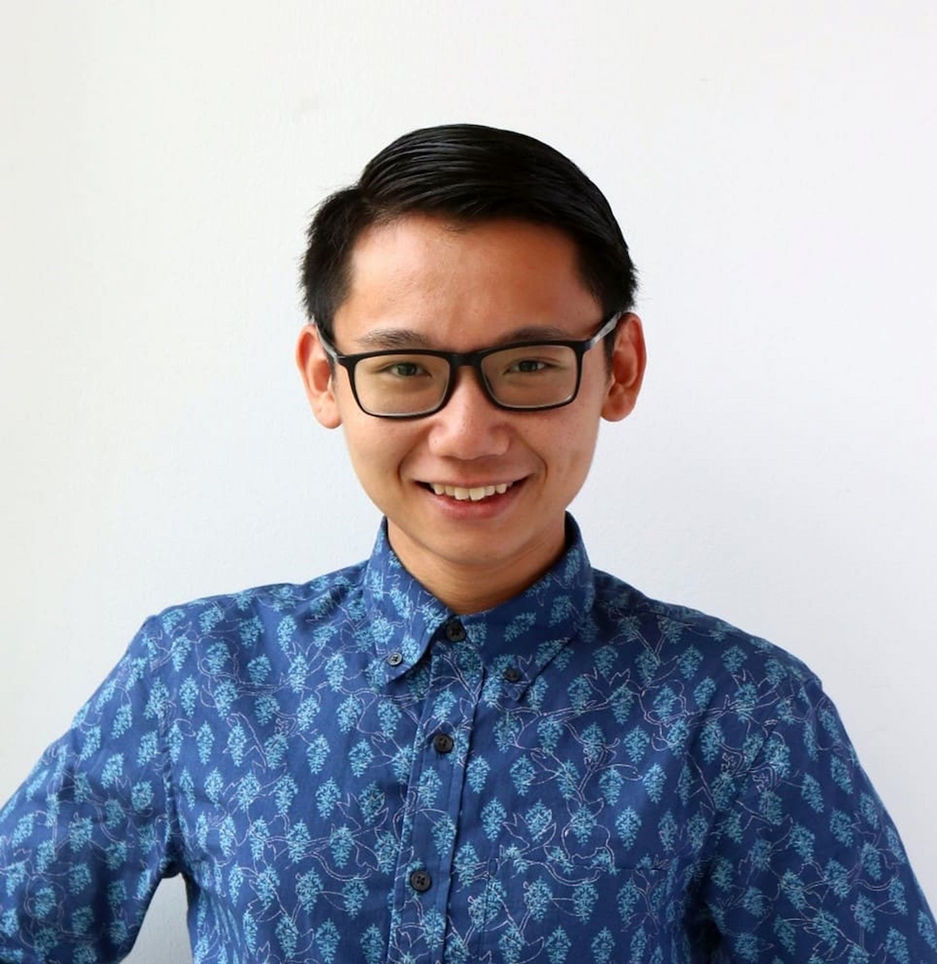 Tak Pham wearing glasses and a blue patterned shirt against a white background.