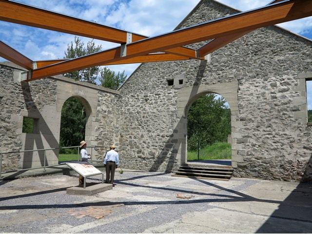Stone ruins with arched windows at Leitch Collieries, visitors reading a display amid scenic greenery.