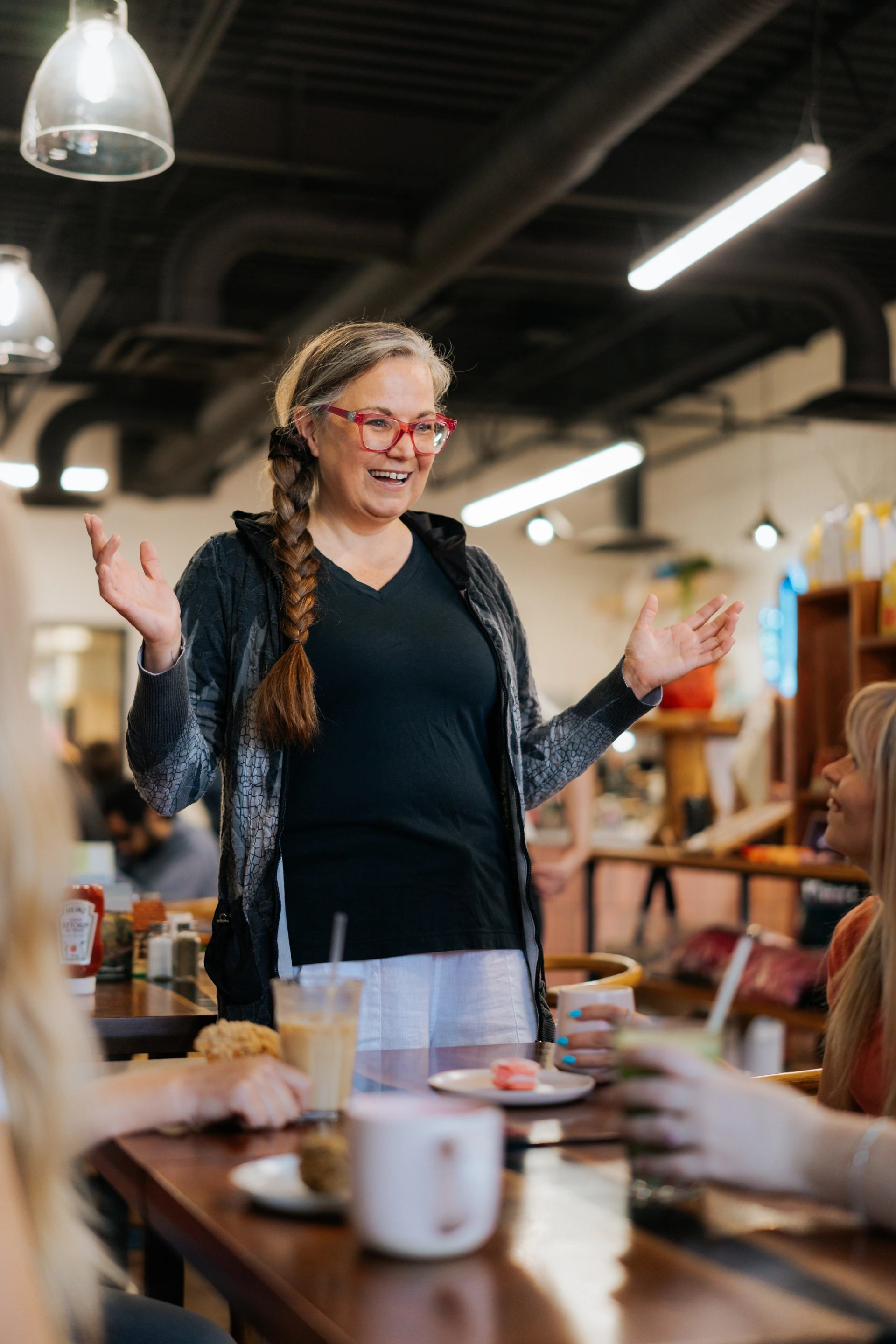 Guide speaking to guests seated at a cafe table with drinks and baked goods in a warm, modern market setting.