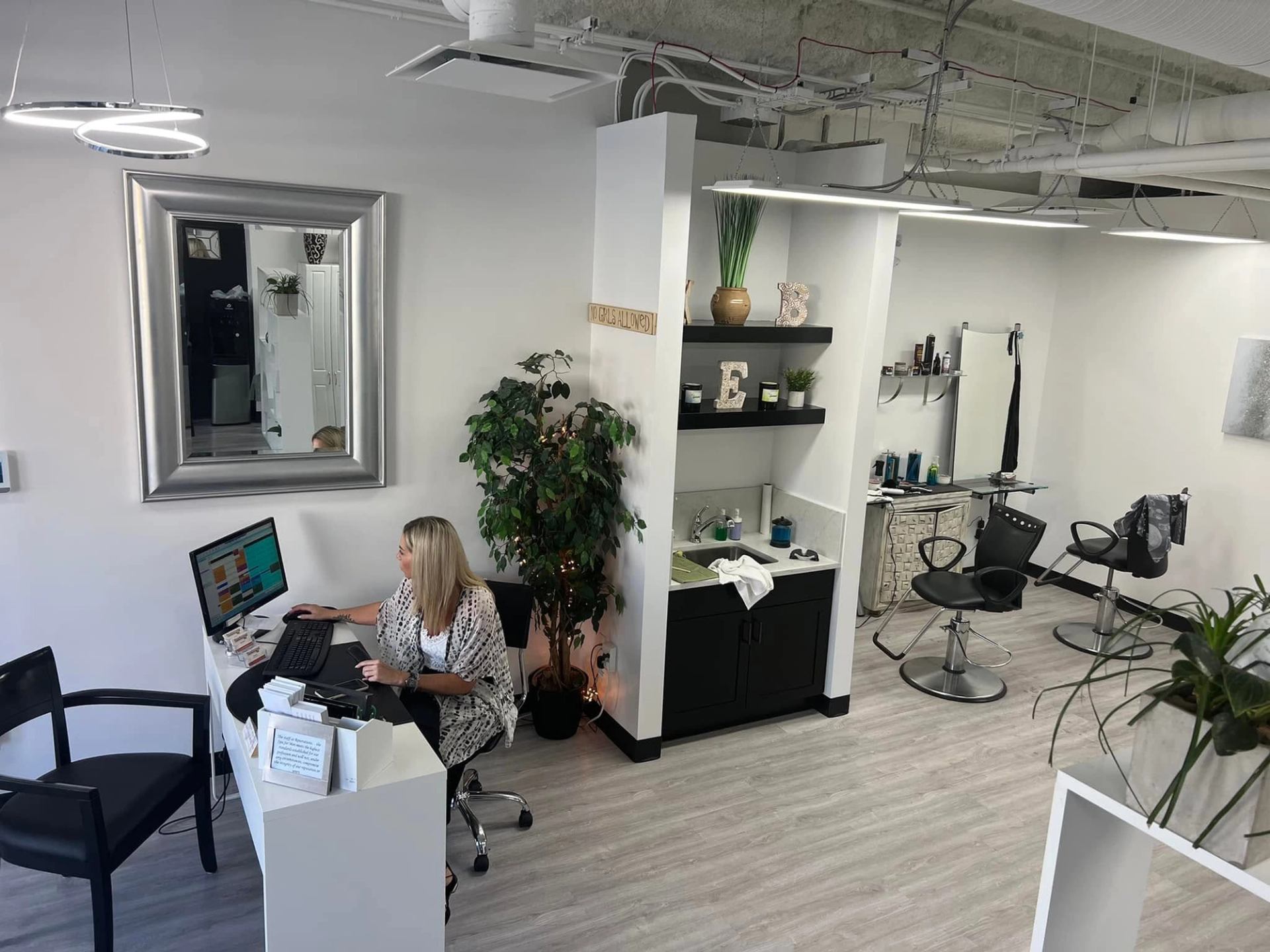 Modern hair salon interior with receptionist at computer and styling stations in background.