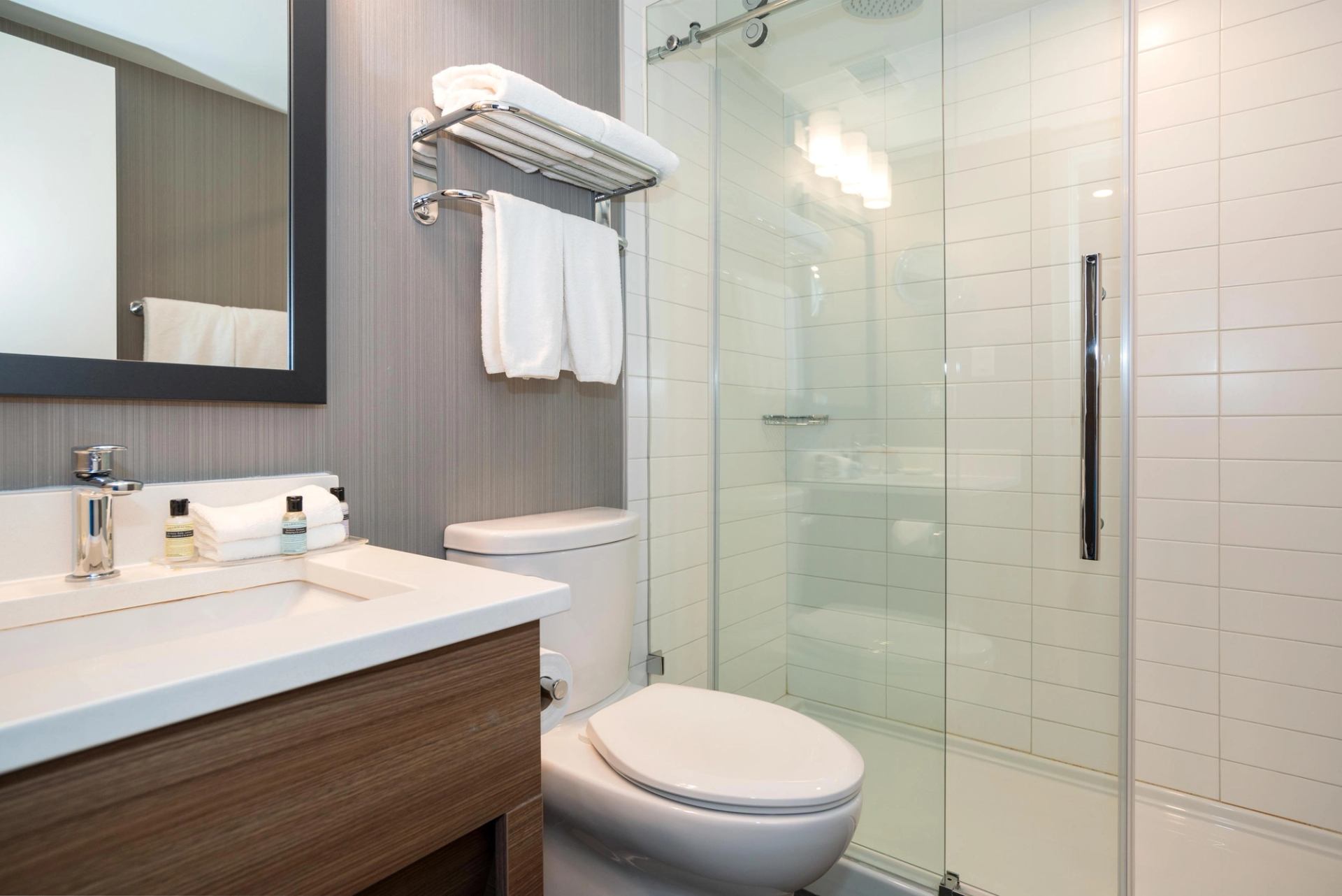 Modern bathroom with vanity, toilet, glass shower enclosure and folded white towels.