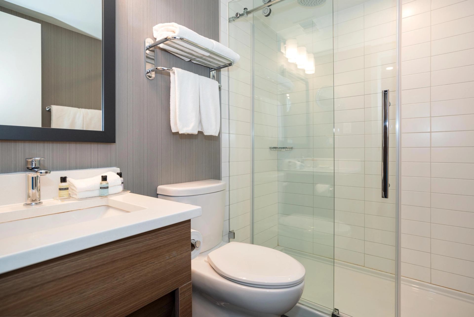 Modern bathroom with vanity, toilet, glass shower enclosure and folded white towels.