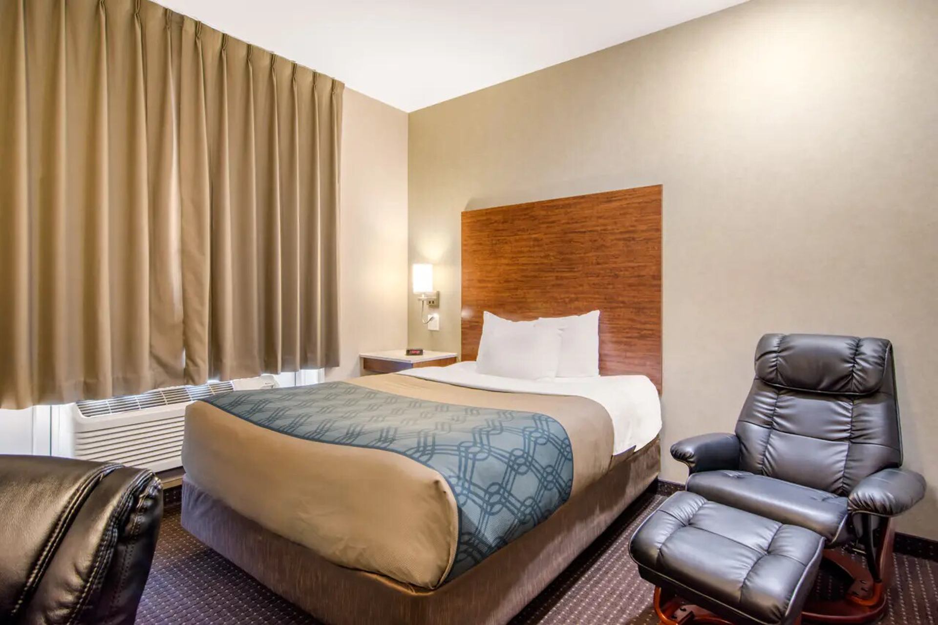 Guest room with queen bed, armchair, and neutral decor at Albertan Inn