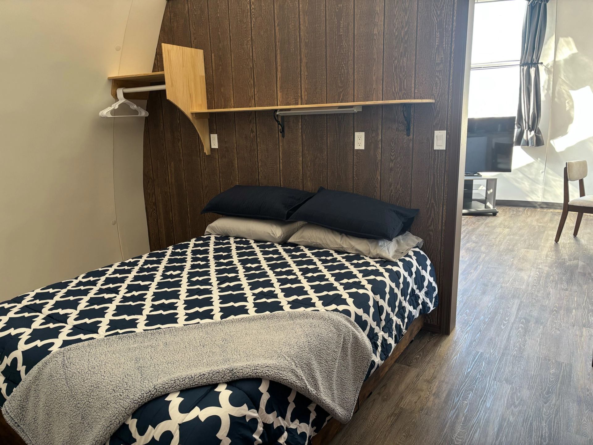 Dome bedroom with patterned bedding, shelf, and open closet.