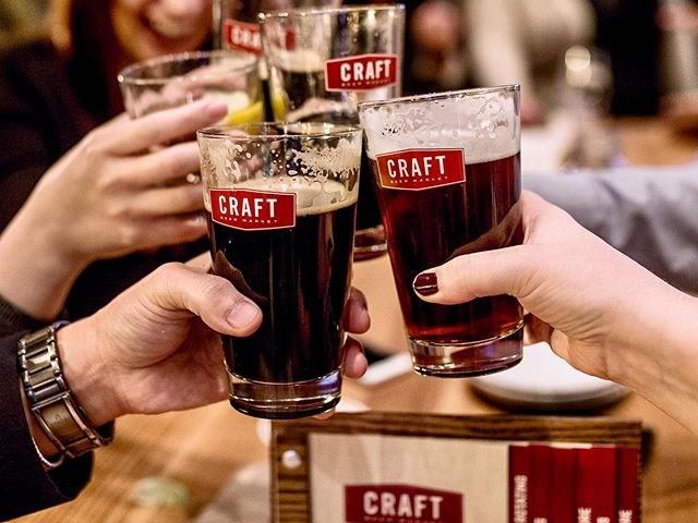 Group toasting with pints of dark craft beer at CRAFT Beer Market.