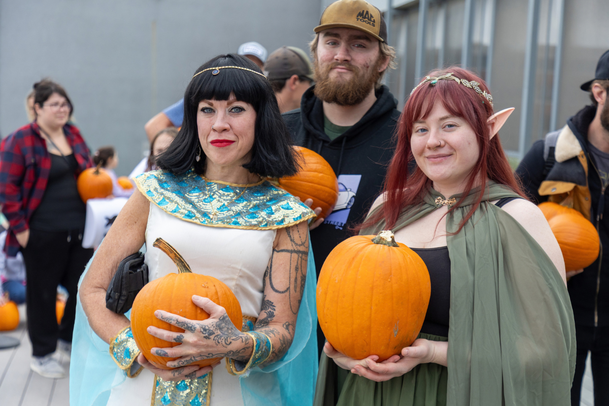 Costumed people hold pumpkins while posing in a crowd.