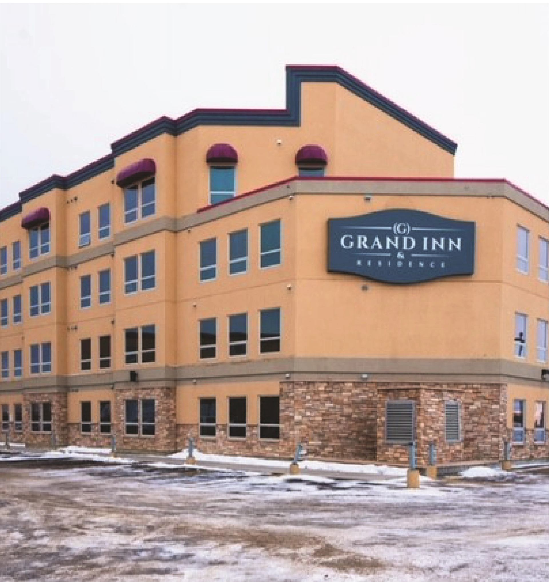 Exterior view of Grand Inn & Residence with tan walls and stone accents in winter setting.