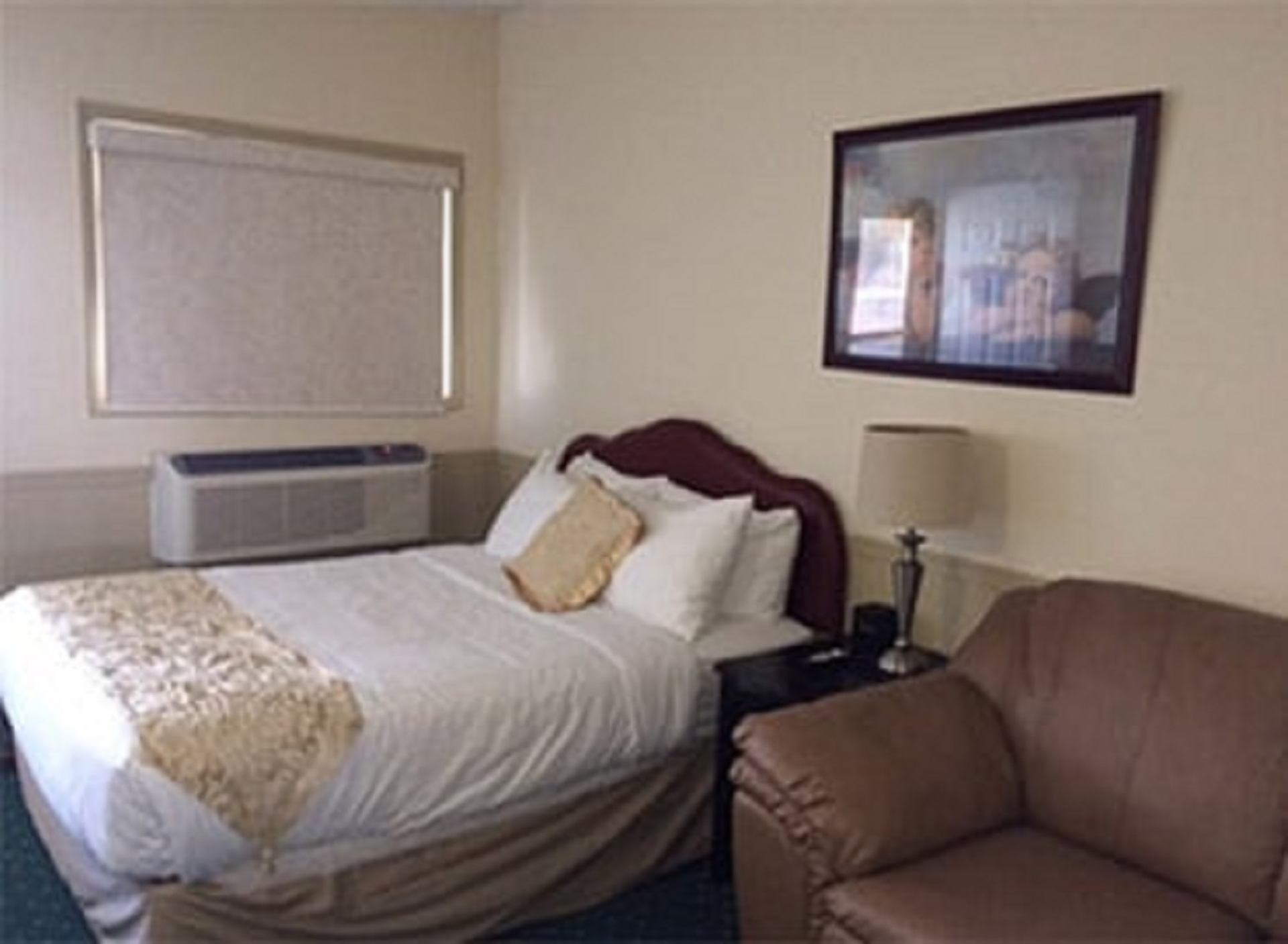 Guest room with neatly made bed, accent pillows, lounge chair, wall art, and air conditioning unit at Centre Suite Inns.