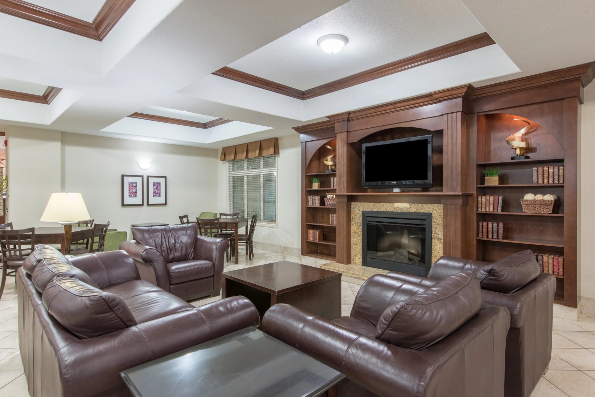 Hotel lounge with brown leather sofas, fireplace, wall-mounted television and bookshelves.