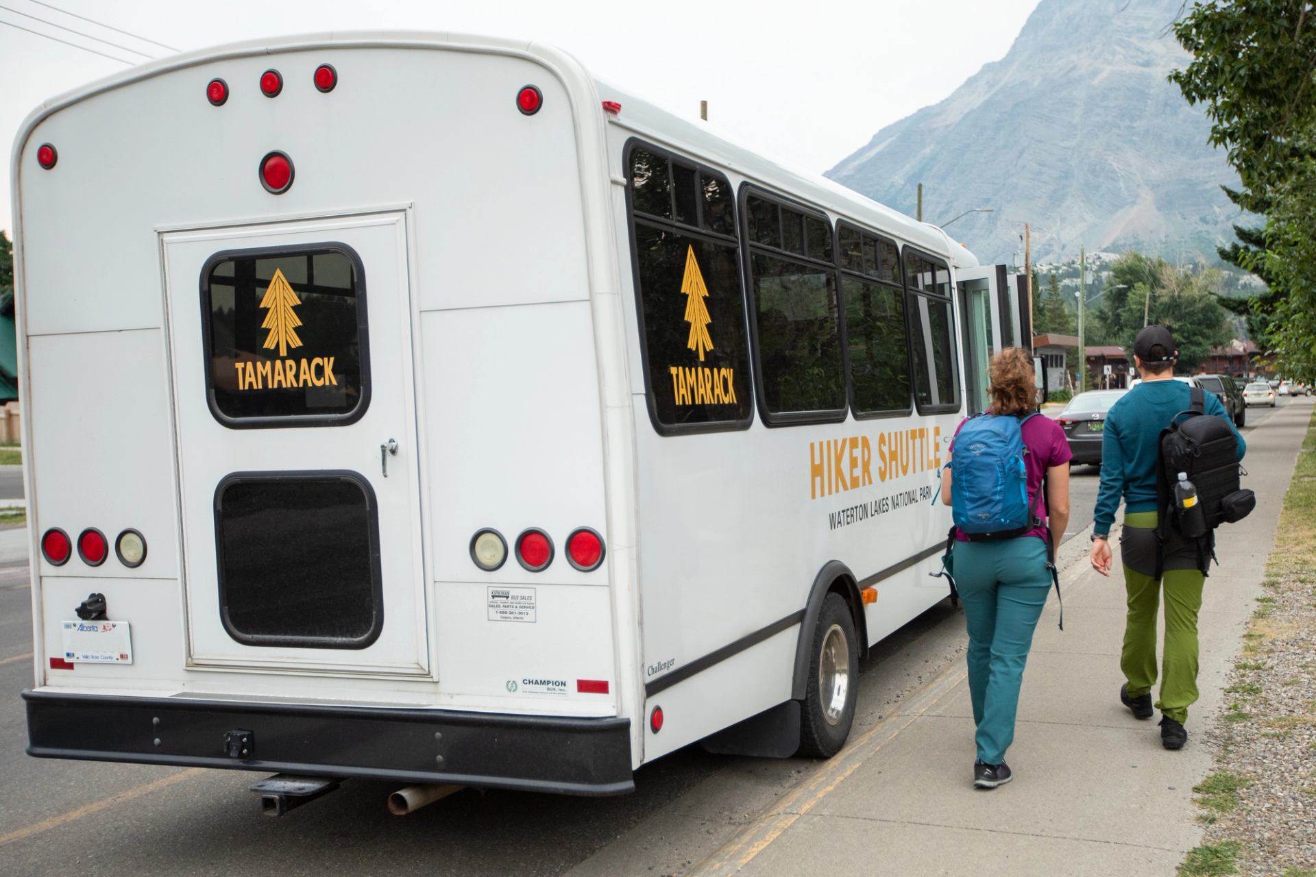 Two hikers walk past a Tamarack hiker shuttle parked roadside in Waterton.