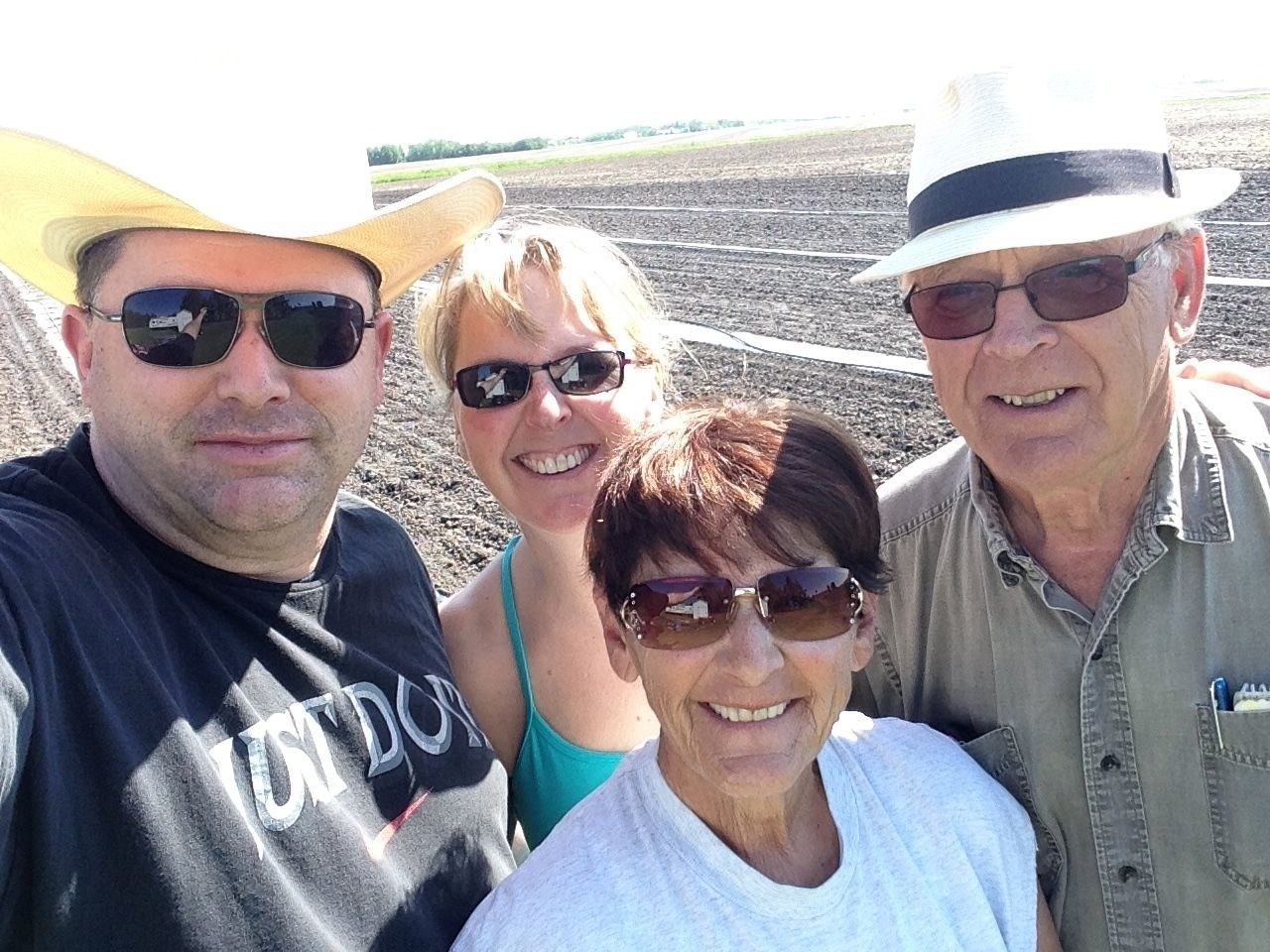 Four people wearing sunglasses pose together in front of a large plowed field.