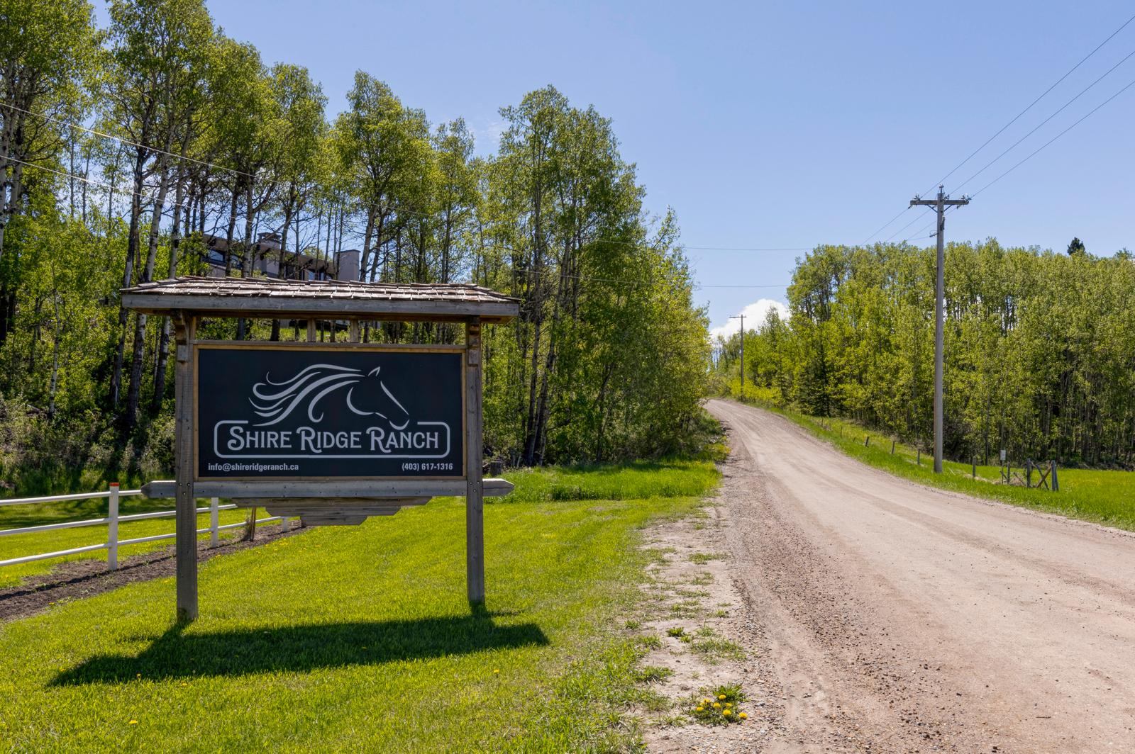 Shire Ridge Ranch entrance sign beside gravel road and green trees under clear sky.