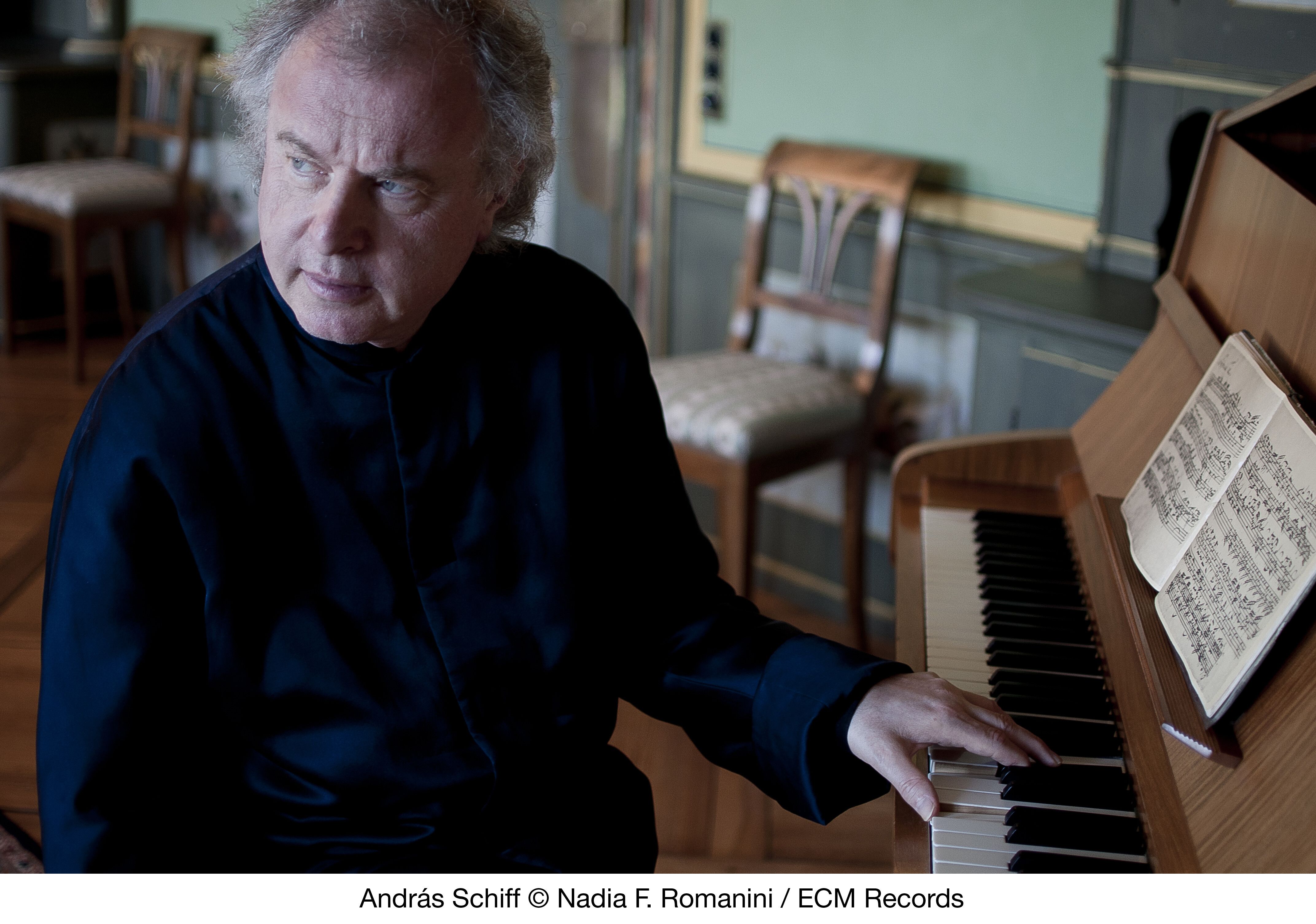 Pianist in dark clothing plays upright piano with open sheet music in quiet room.