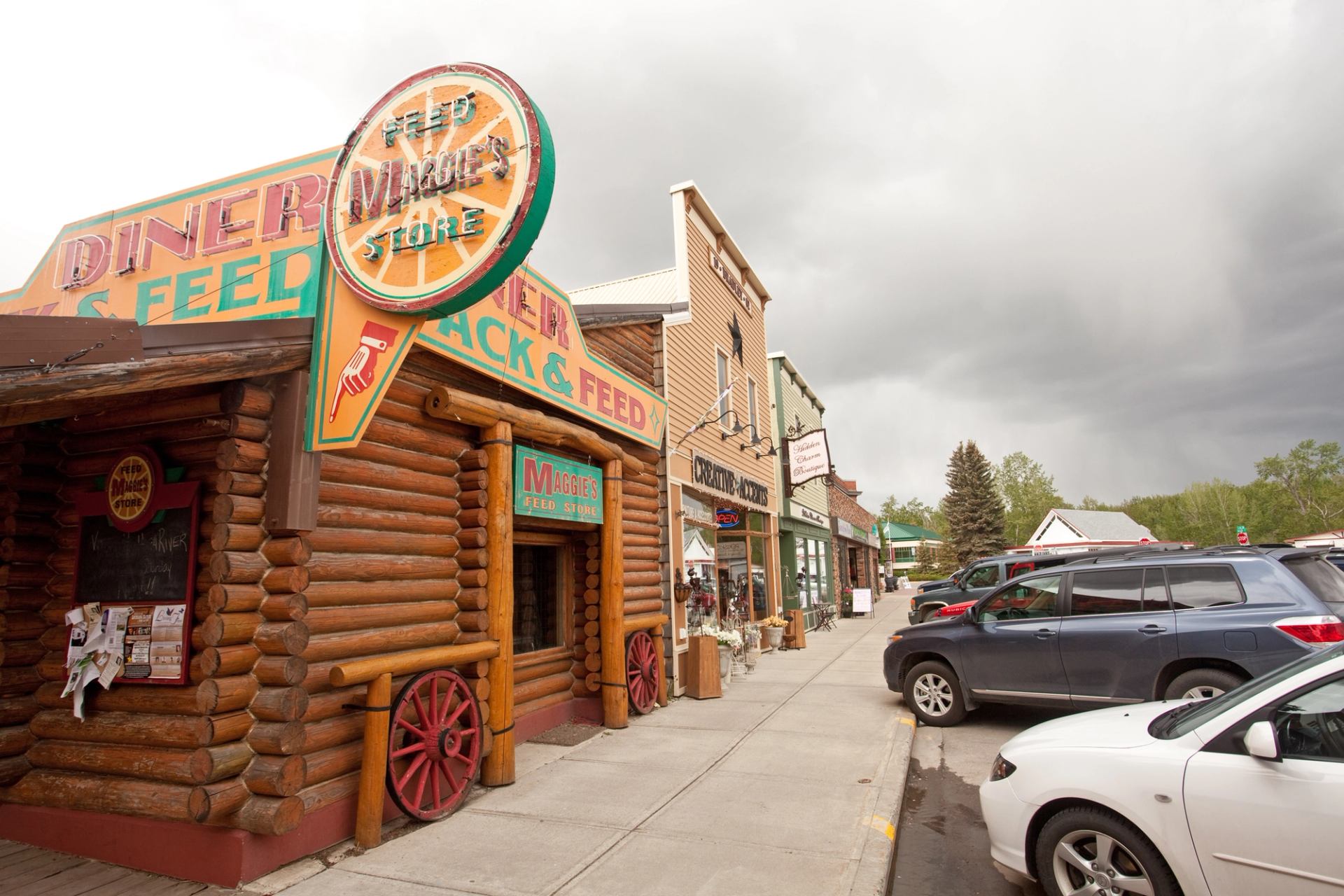 Small-town main street with Maggie’s Feed Store, wooden storefronts and parked cars.