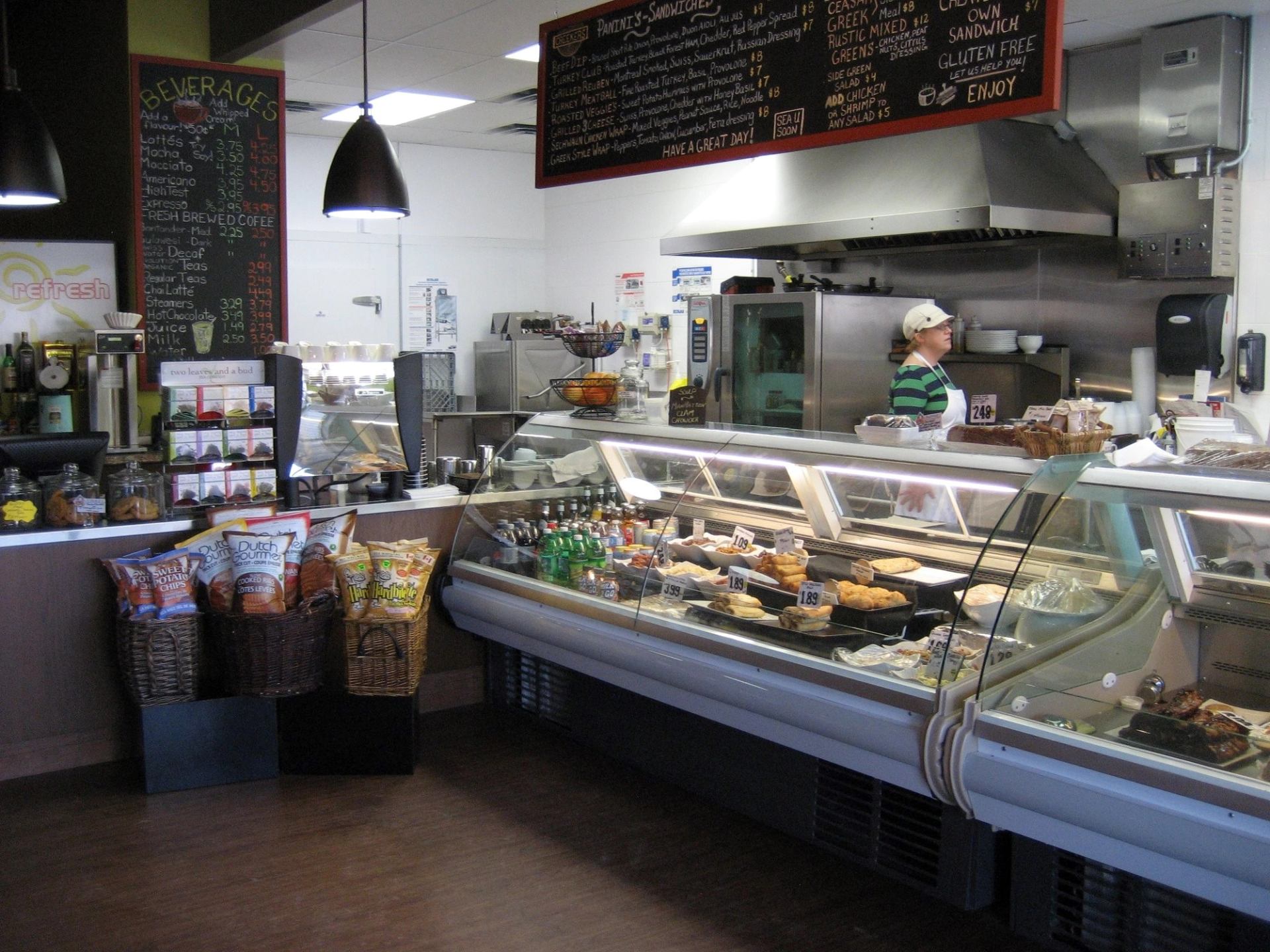 Deli counter with pastries, drinks and menu boards, staff member behind glass case.