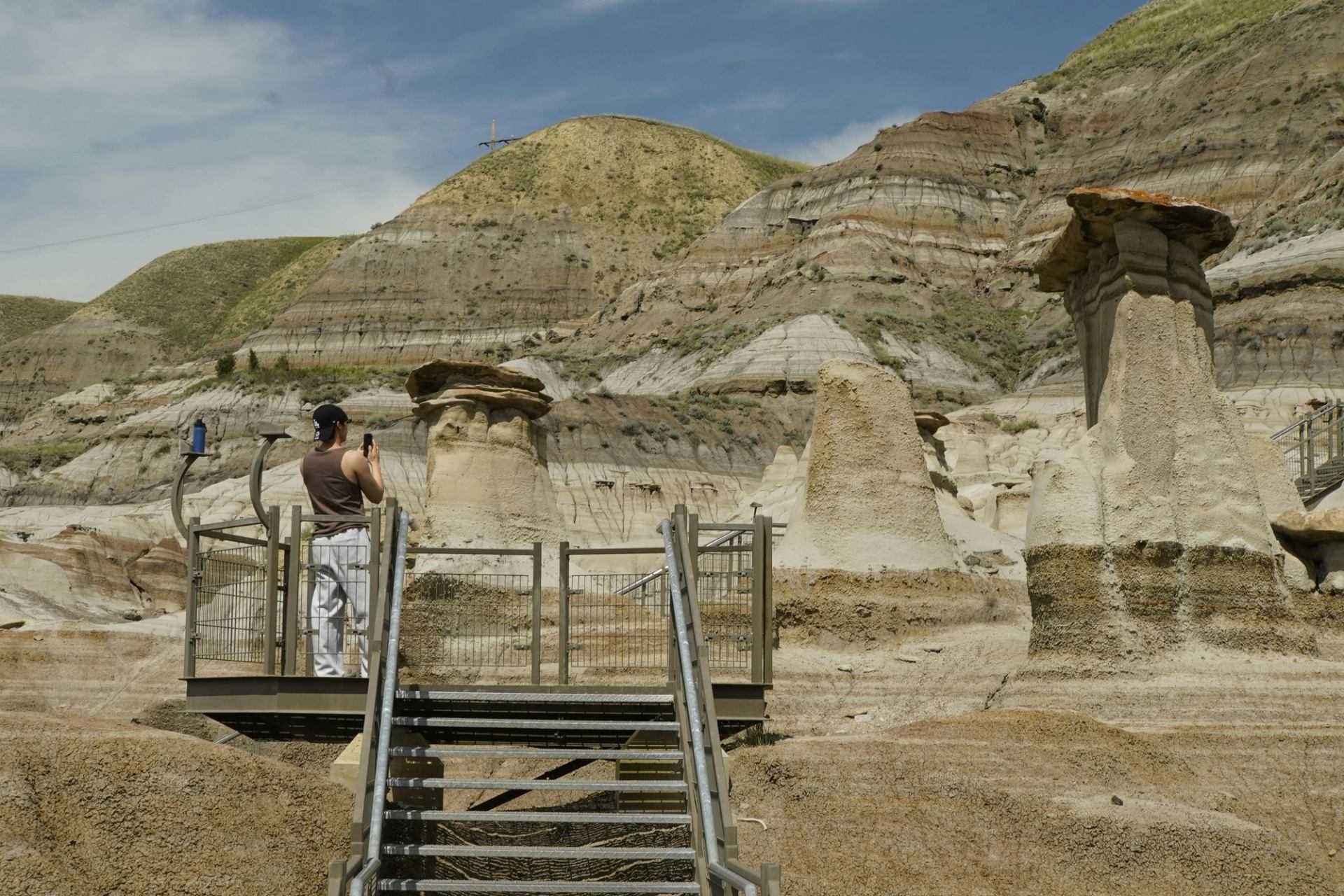 Visitor on viewing platform photographing hoodoos against layered badlands cliffs.