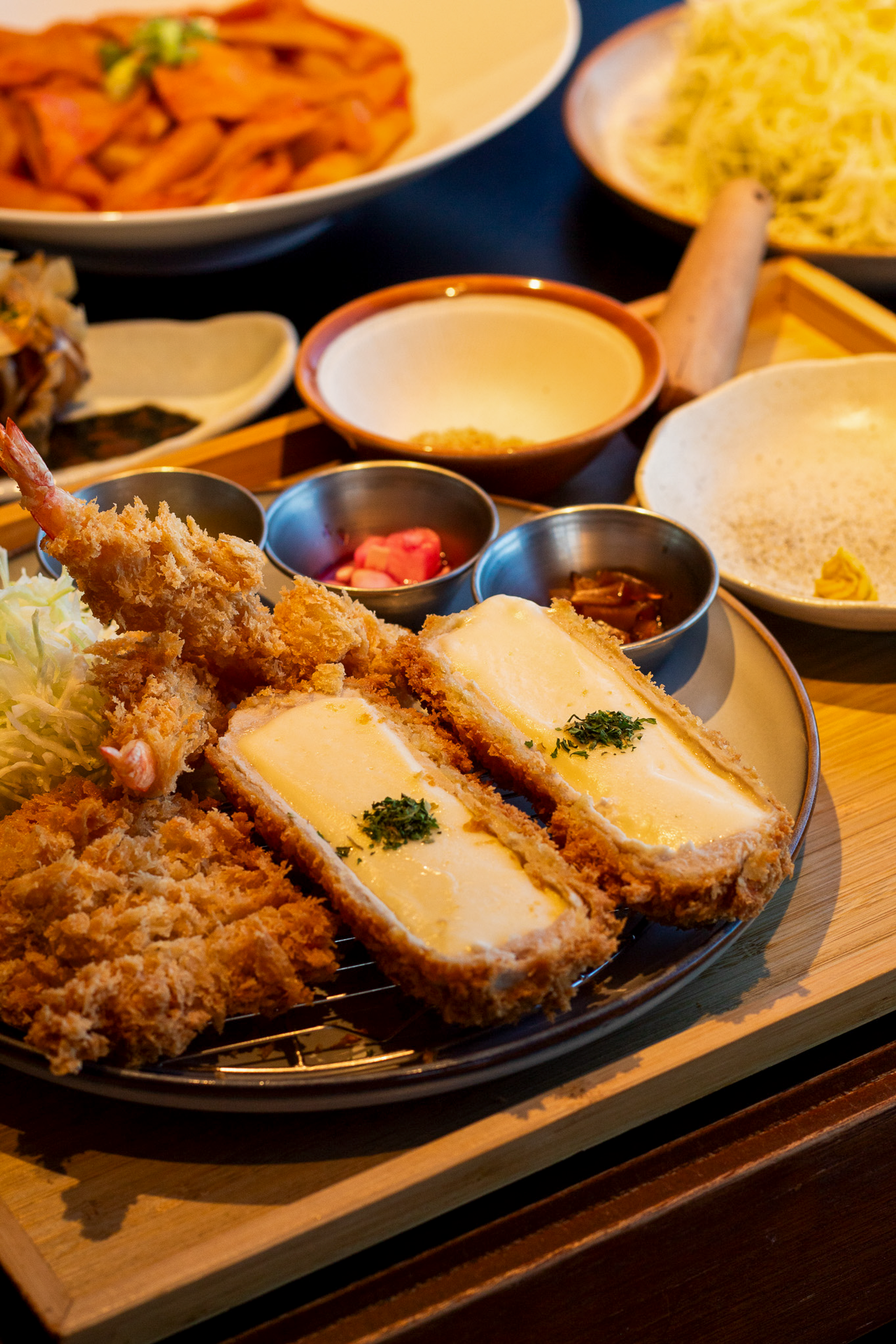 Breaded cutlets with melted cheese, shredded cabbage and small side dishes on wooden tray.