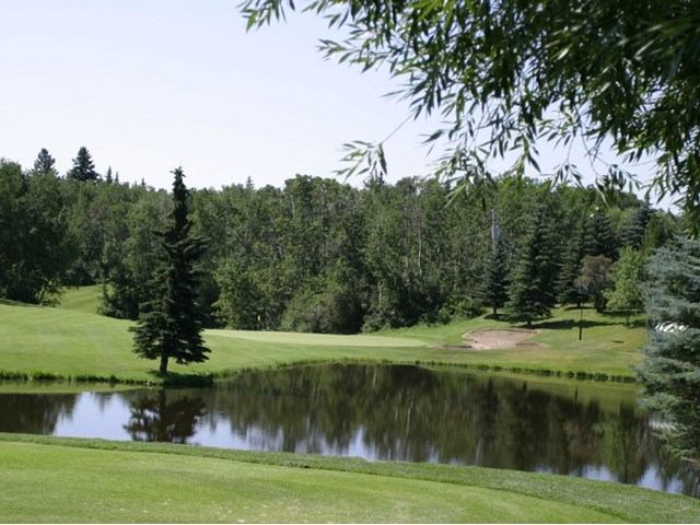 Golf course view with pond, green fairway, and surrounding trees at Lacombe Golf and Country Club.