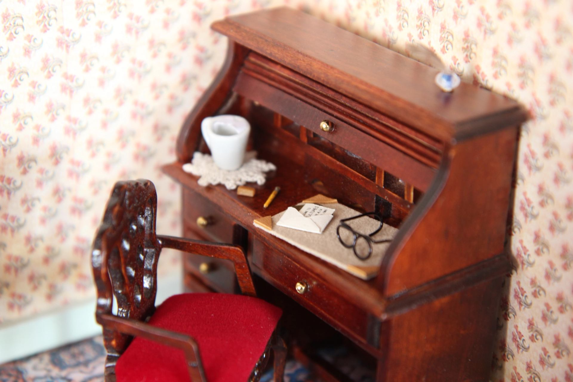 Copilot said:  Miniature roll-top desk with glasses, papers, cup, and red-cushioned chair.