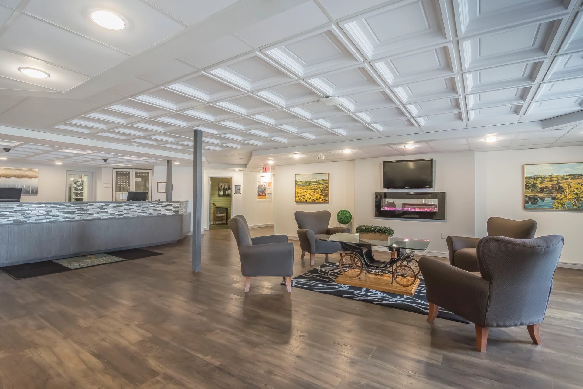 Spacious hotel lobby with cozy gray armchairs around a glass coffee table, modern decor, large wall paintings, and a welcoming ambiance.