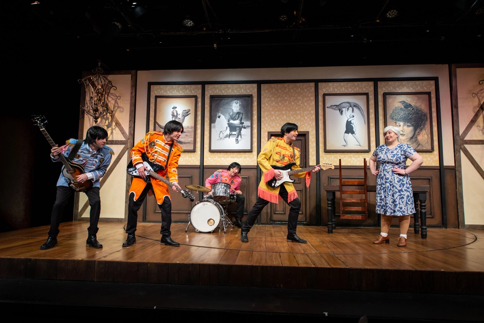 Stage performance with band in colourful uniforms playing instruments beside person in patterned dress.