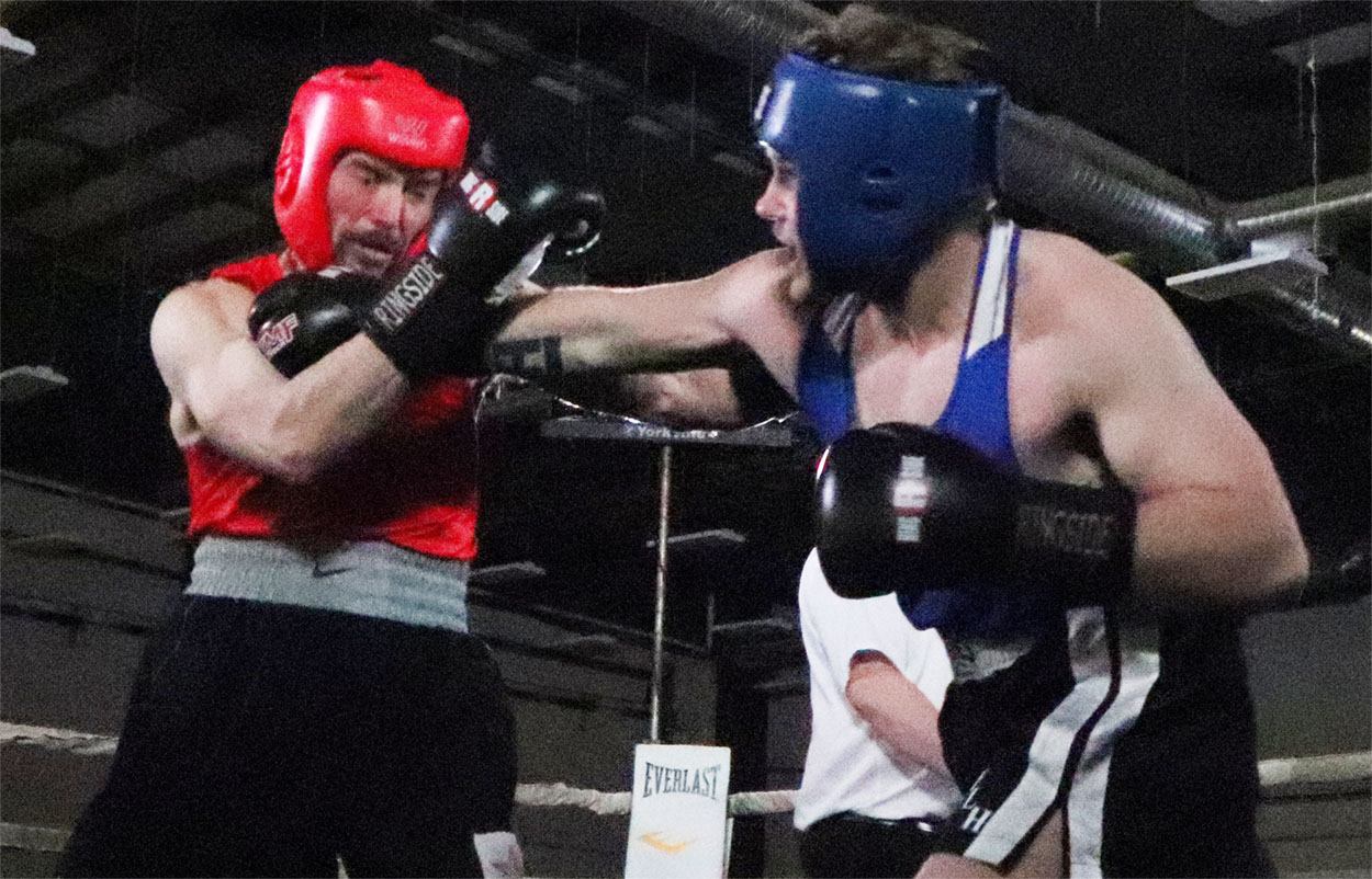 Two boxers in headgear exchange punches in a boxing ring.