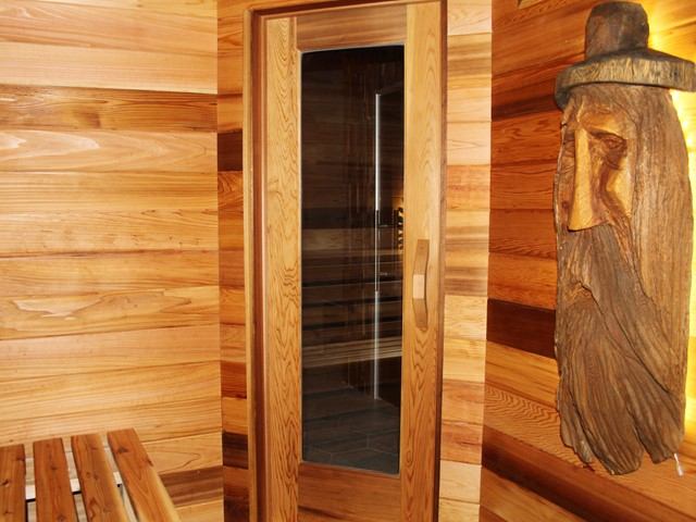 A wooden sauna with a carved face sculpture and a glass door.