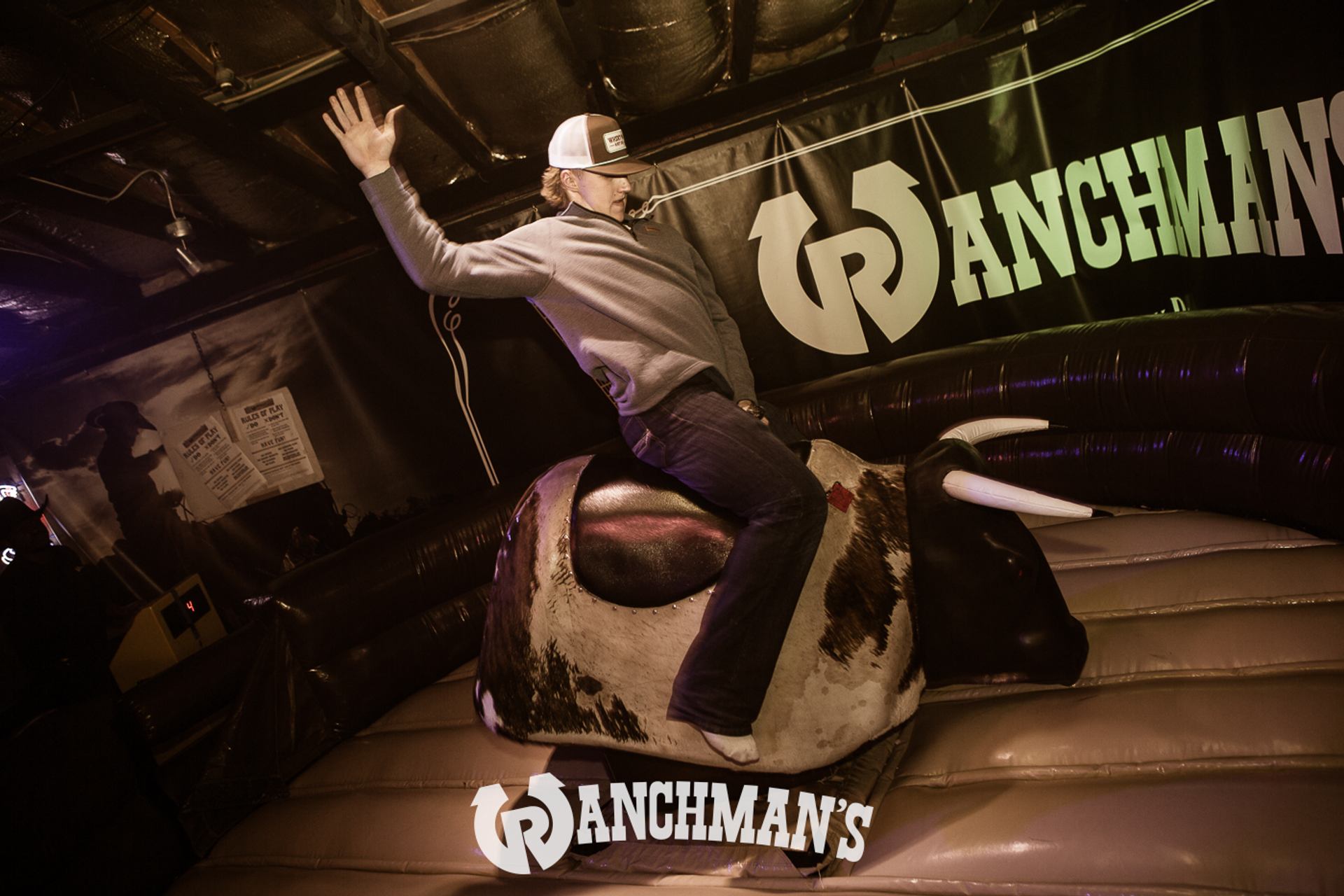 Person rides mechanical bull at Ranchman’s bar, raising one arm for balance.