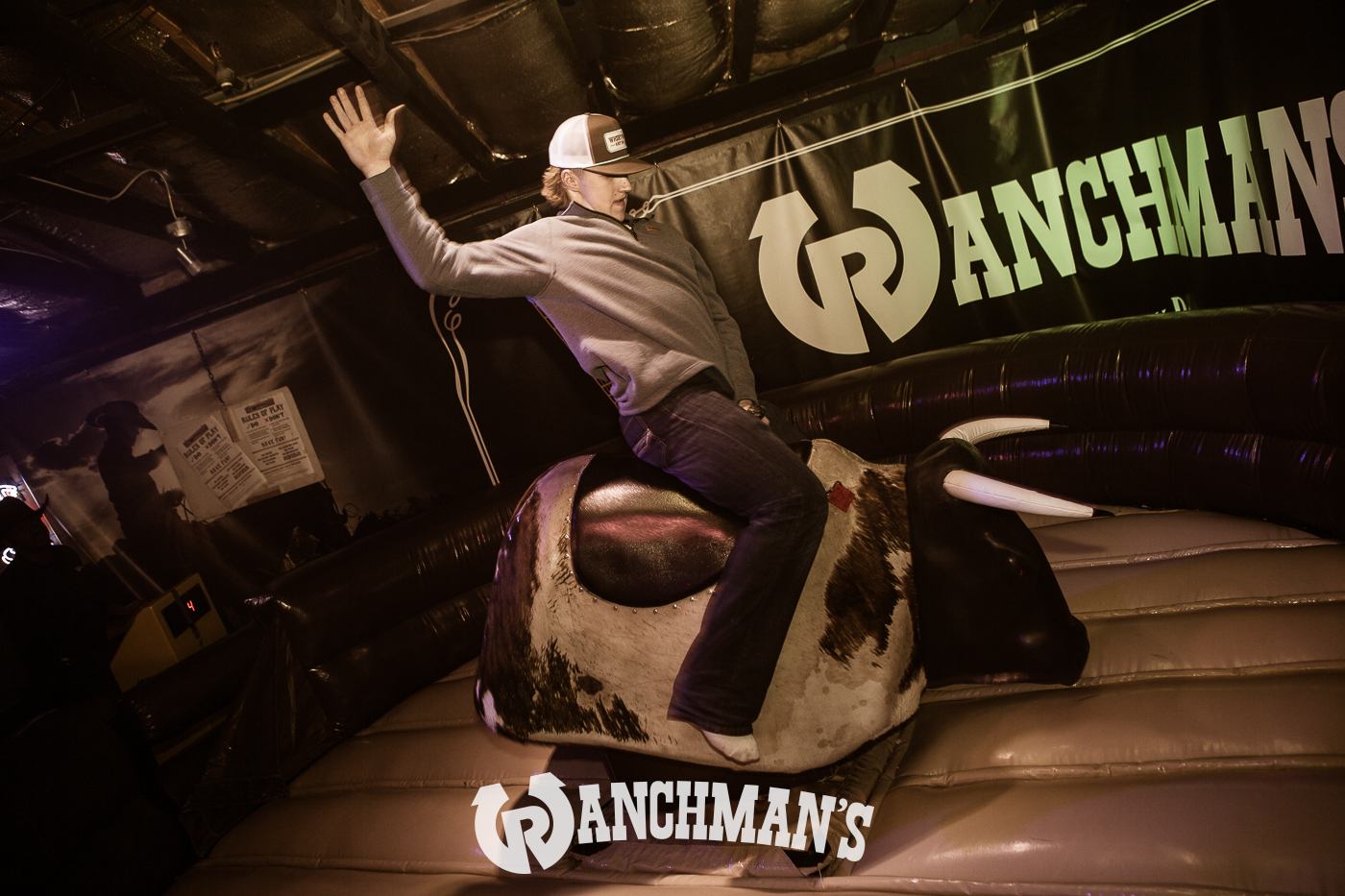 Person rides mechanical bull at Ranchman’s bar, raising one arm for balance.