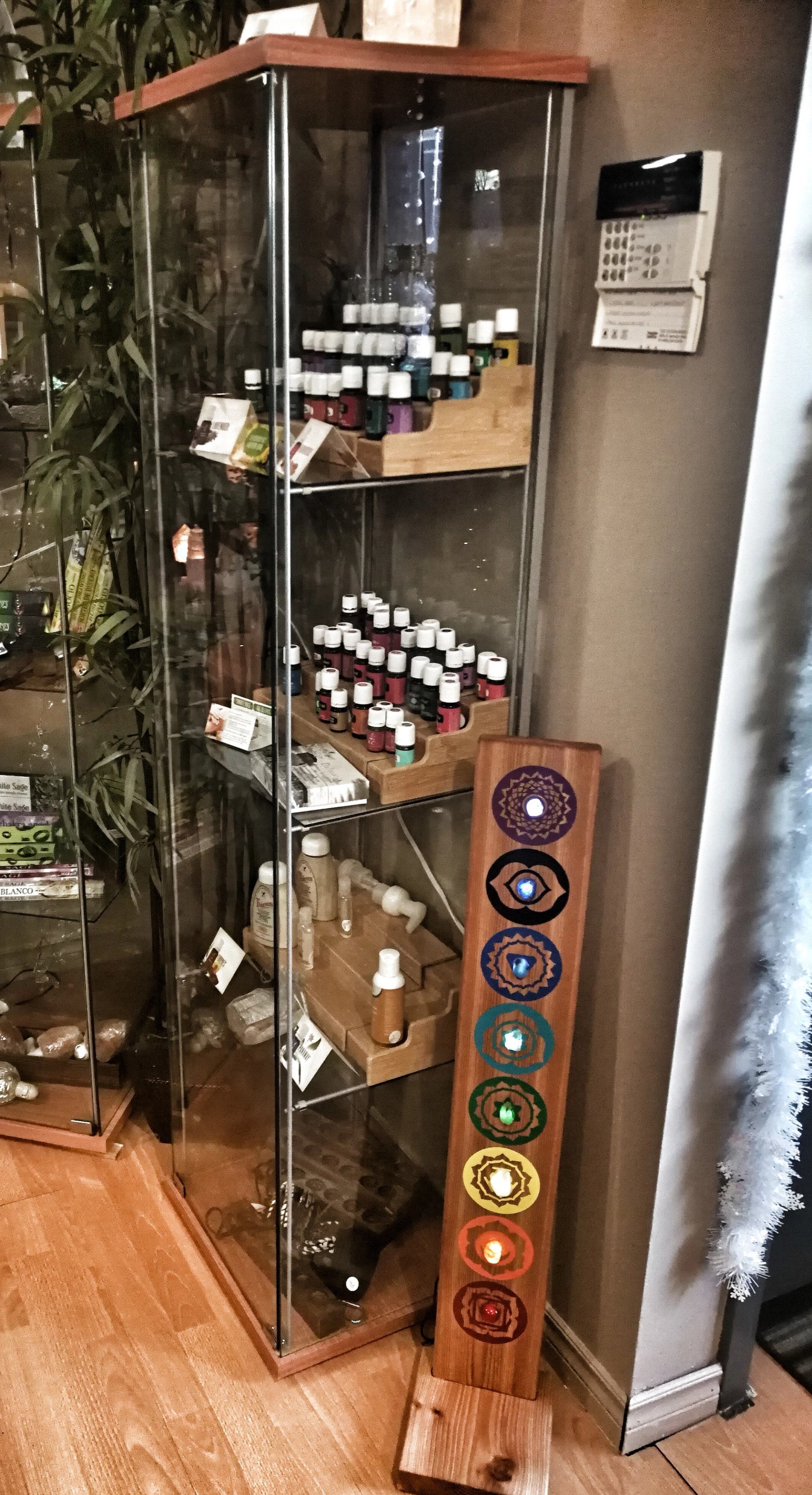 Glass cabinet filled with essential oils and wellness products beside chakra artwork.