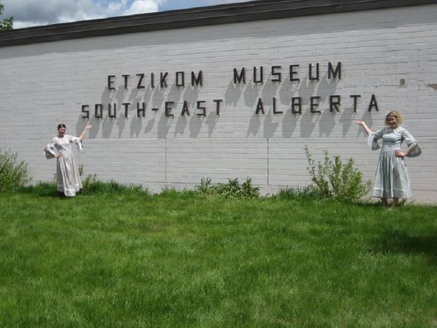 The sign at the Etzikom Museum and Historic Windmill Center, with two women dressed in historic clothing on either side.