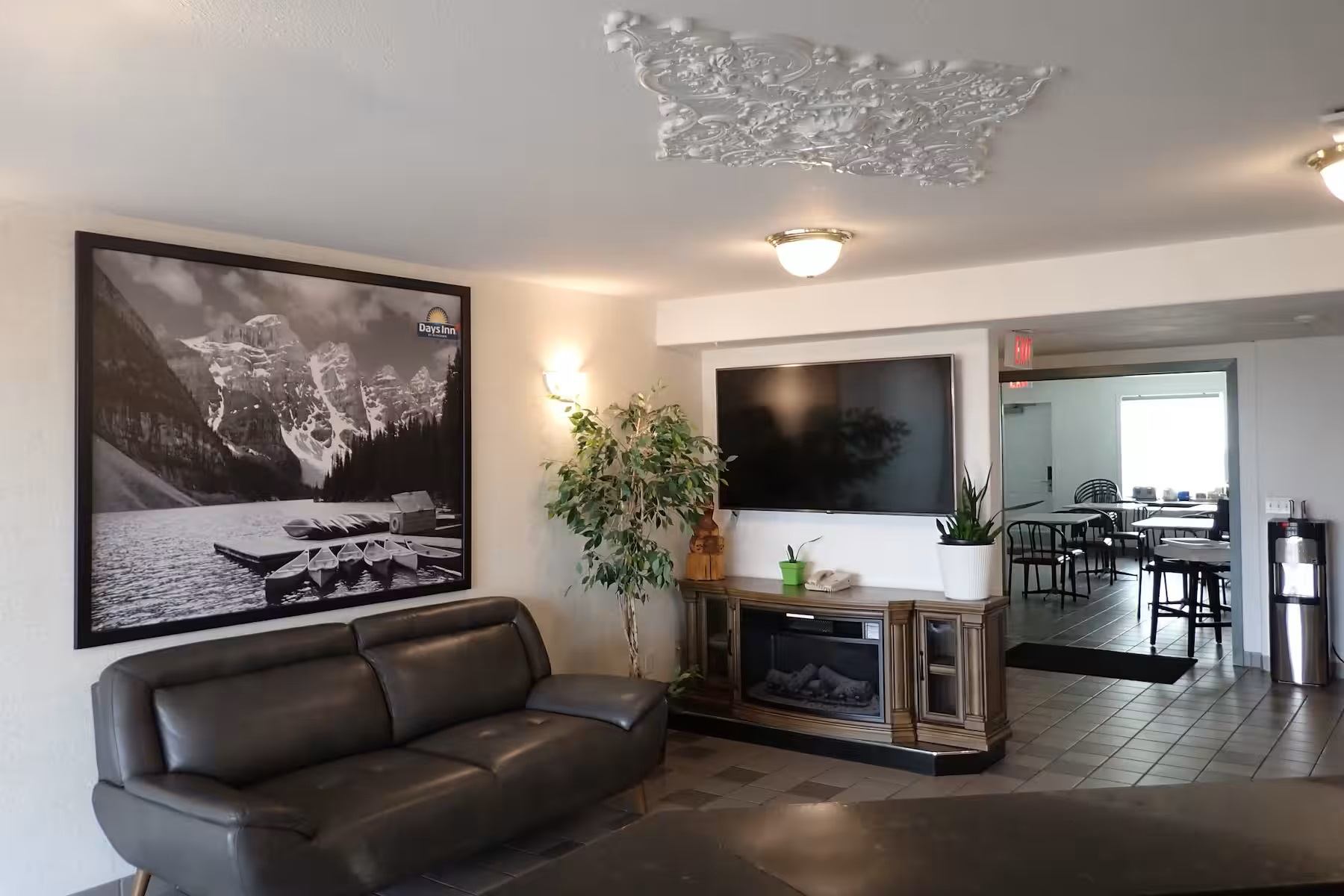 Lobby with leather seating, framed mountain photo, fireplace, TV, plants, and a dining area in the back.